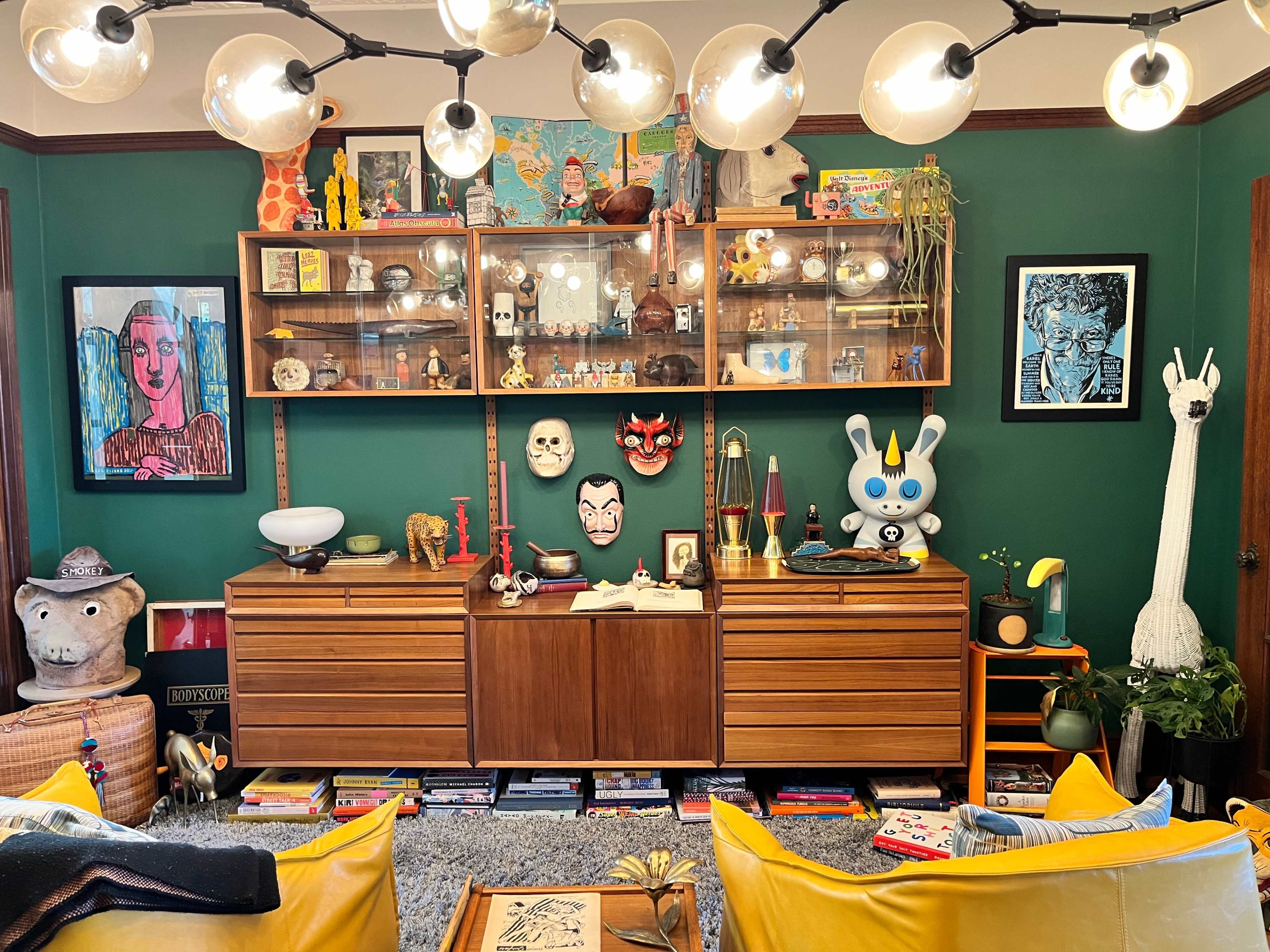 A vibrant living room with a green wall, showcasing a wooden cabinet filled with various collectibles, framed art, and decorative items, complemented by a cozy seating area.
