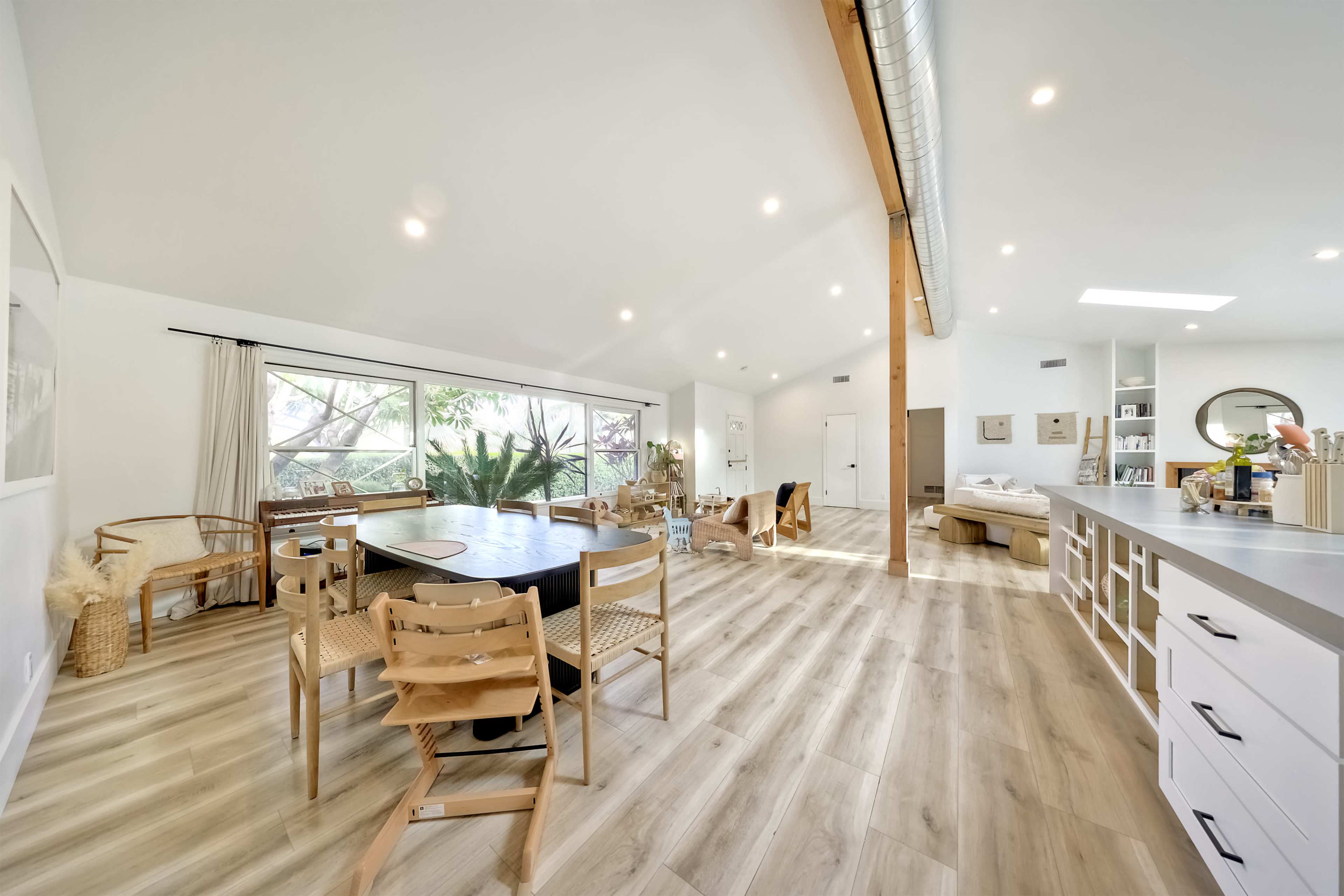 The image features a spacious open-concept living area with a dining table, chairs, and large windows allowing natural light to enter.