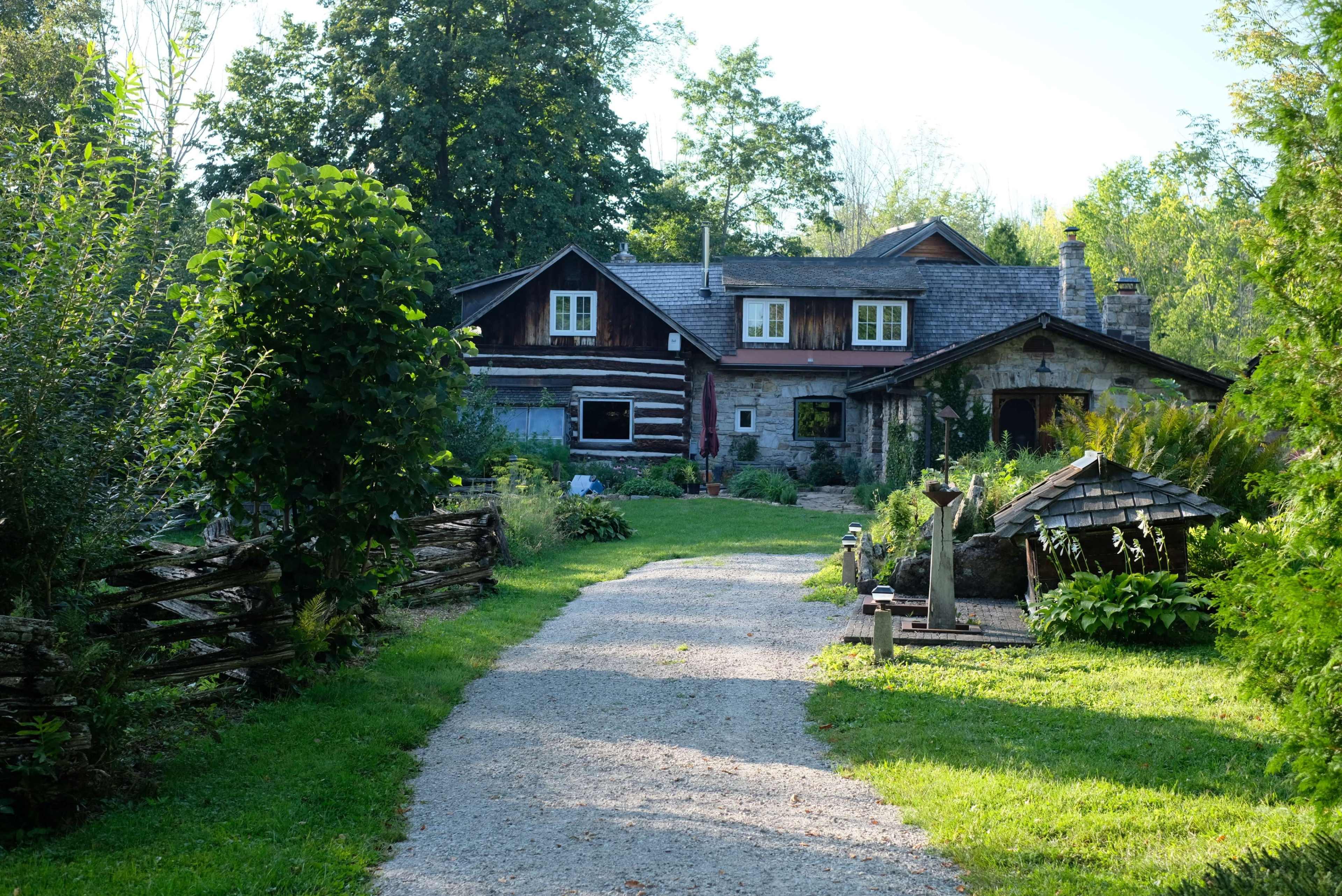 A gravel pathway leads to a rustic house surrounded by greenery and gardens.