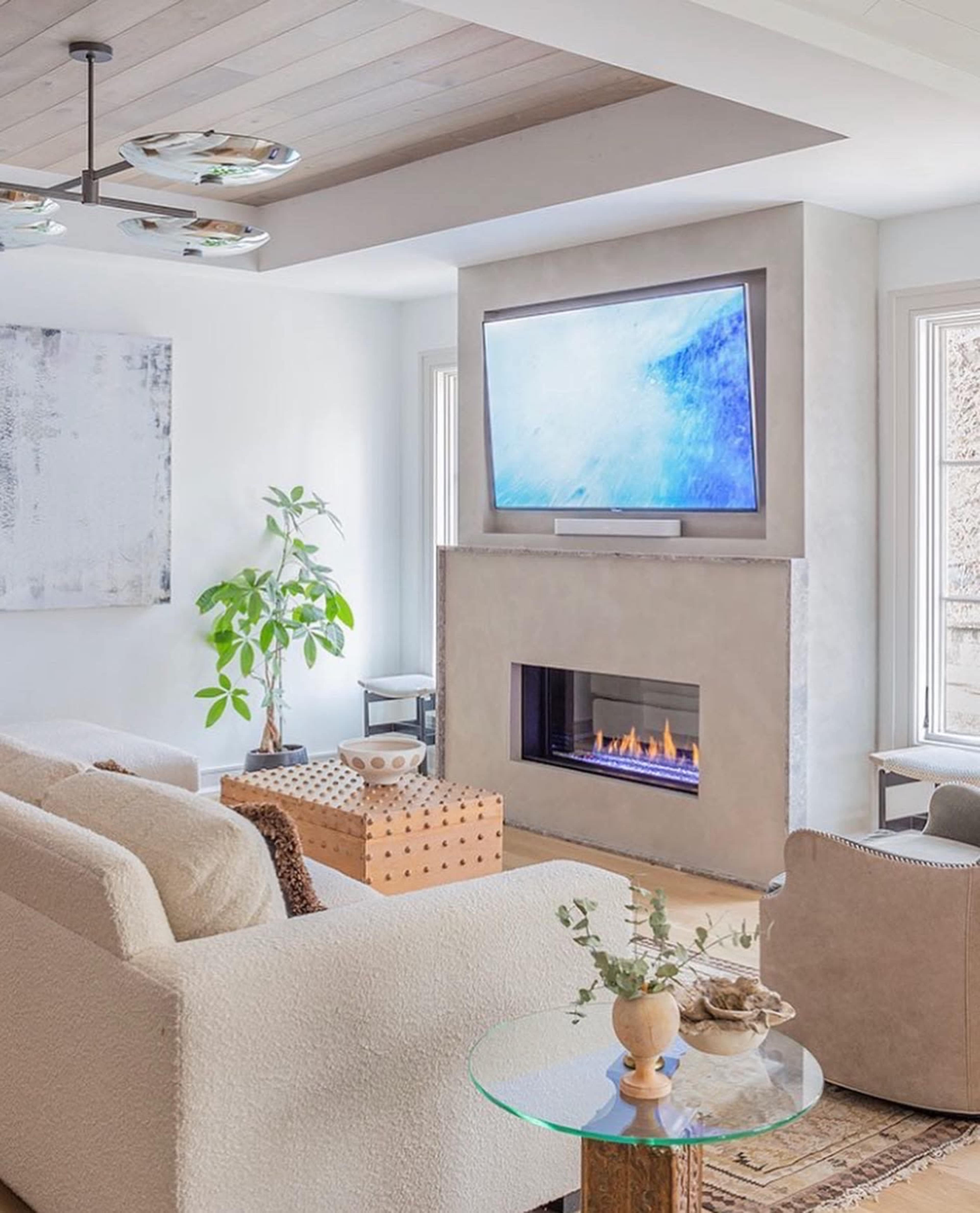 A modern living room featuring a sectional sofa, a wall-mounted television above a sleek fireplace, and a coffee table with decorative items.