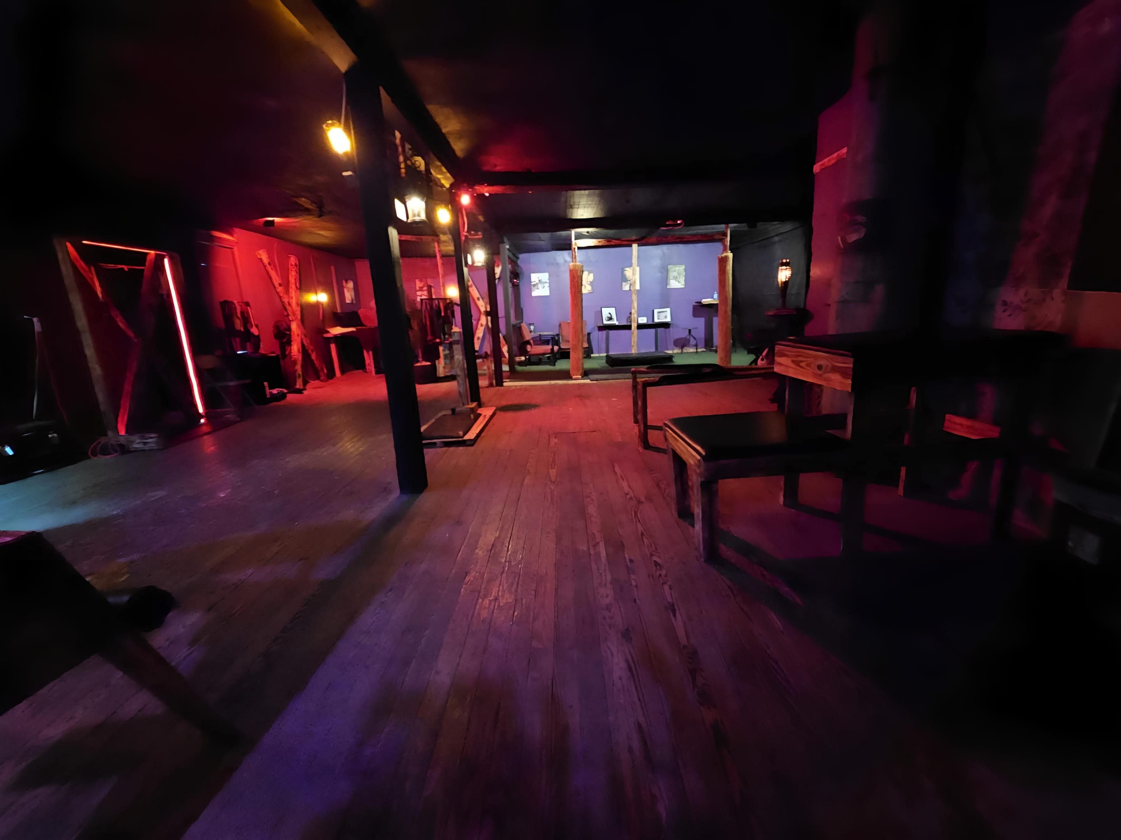 A dimly lit interior with wooden flooring, tables, and colorful lighting effects creating a moody atmosphere.