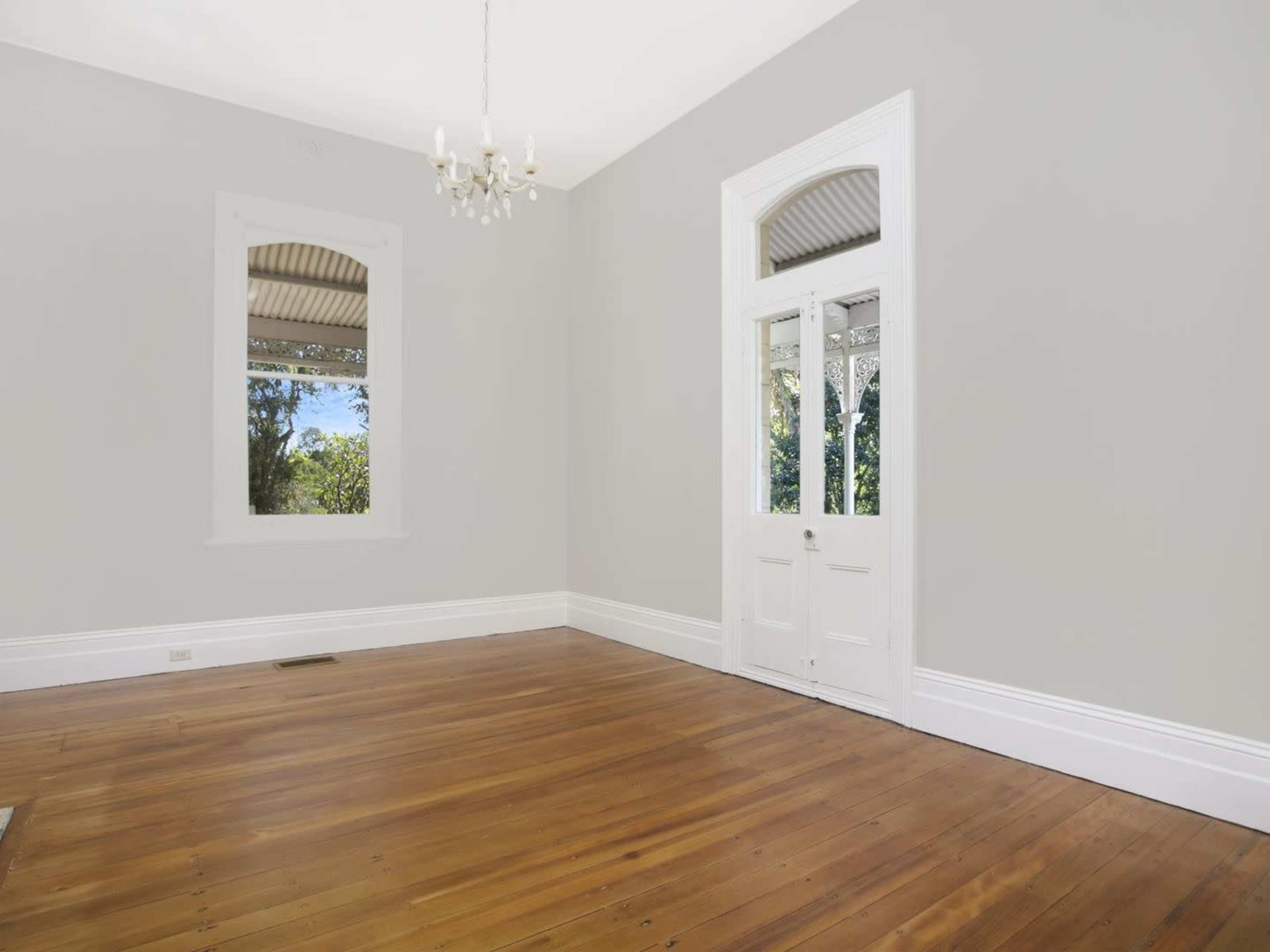 The room features light gray walls, wooden flooring, a chandelier, and large windows with a door leading outside.