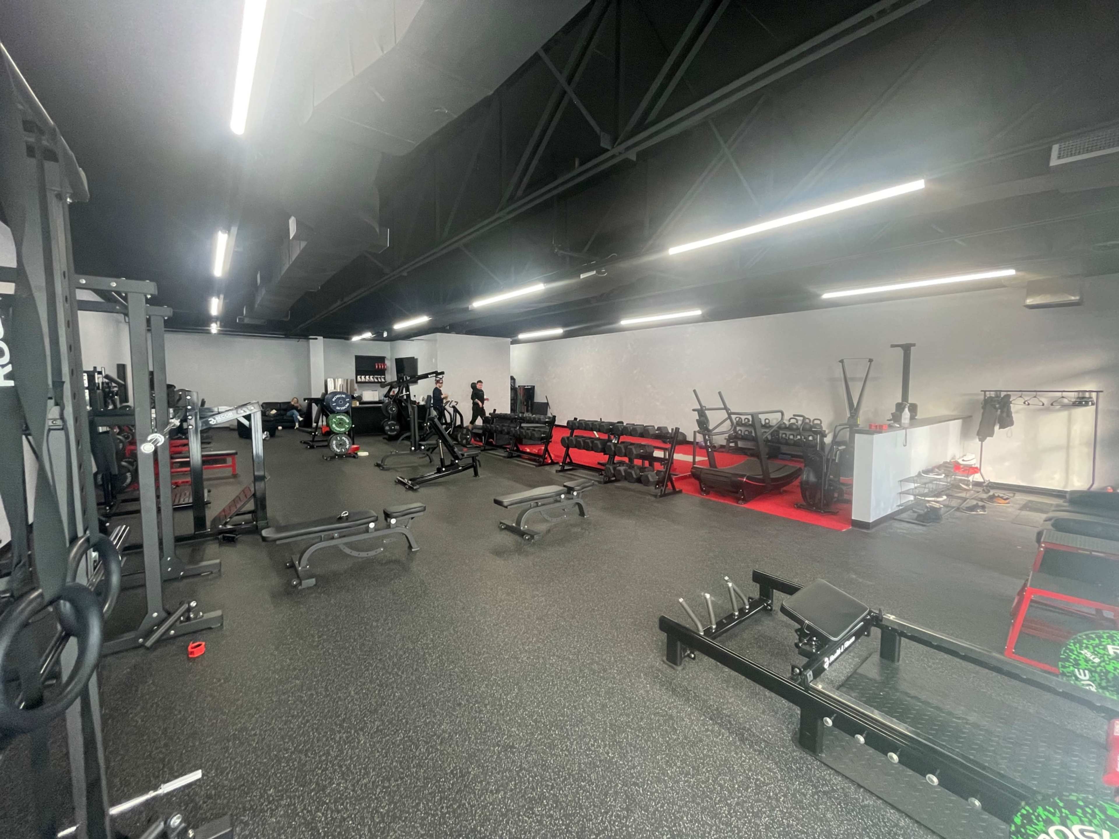 A spacious gym filled with various workout equipment, including weights and machines, under fluorescent lighting.