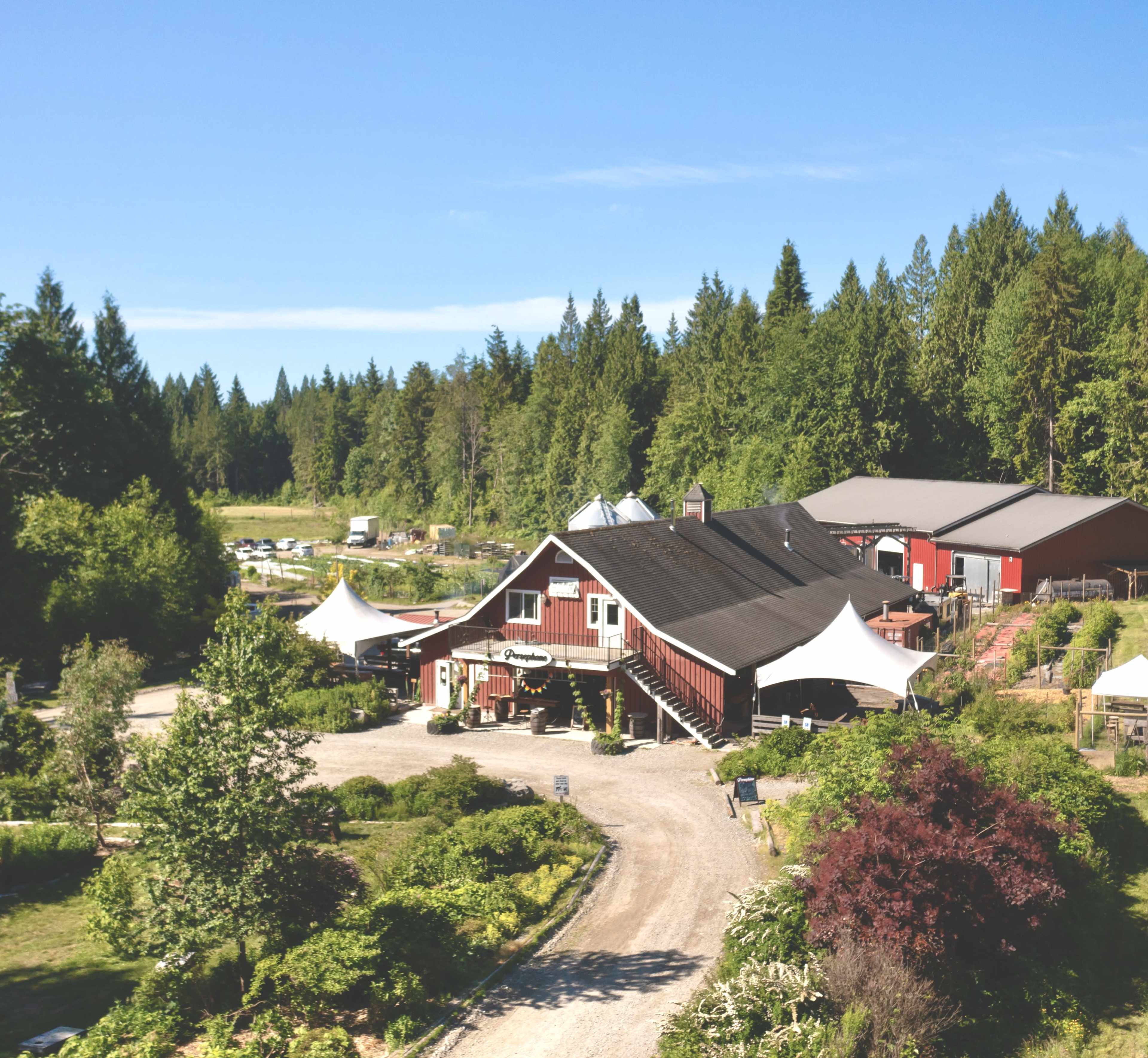 A red barn-style building surrounded by gardens and trees, with white tents set up outside.