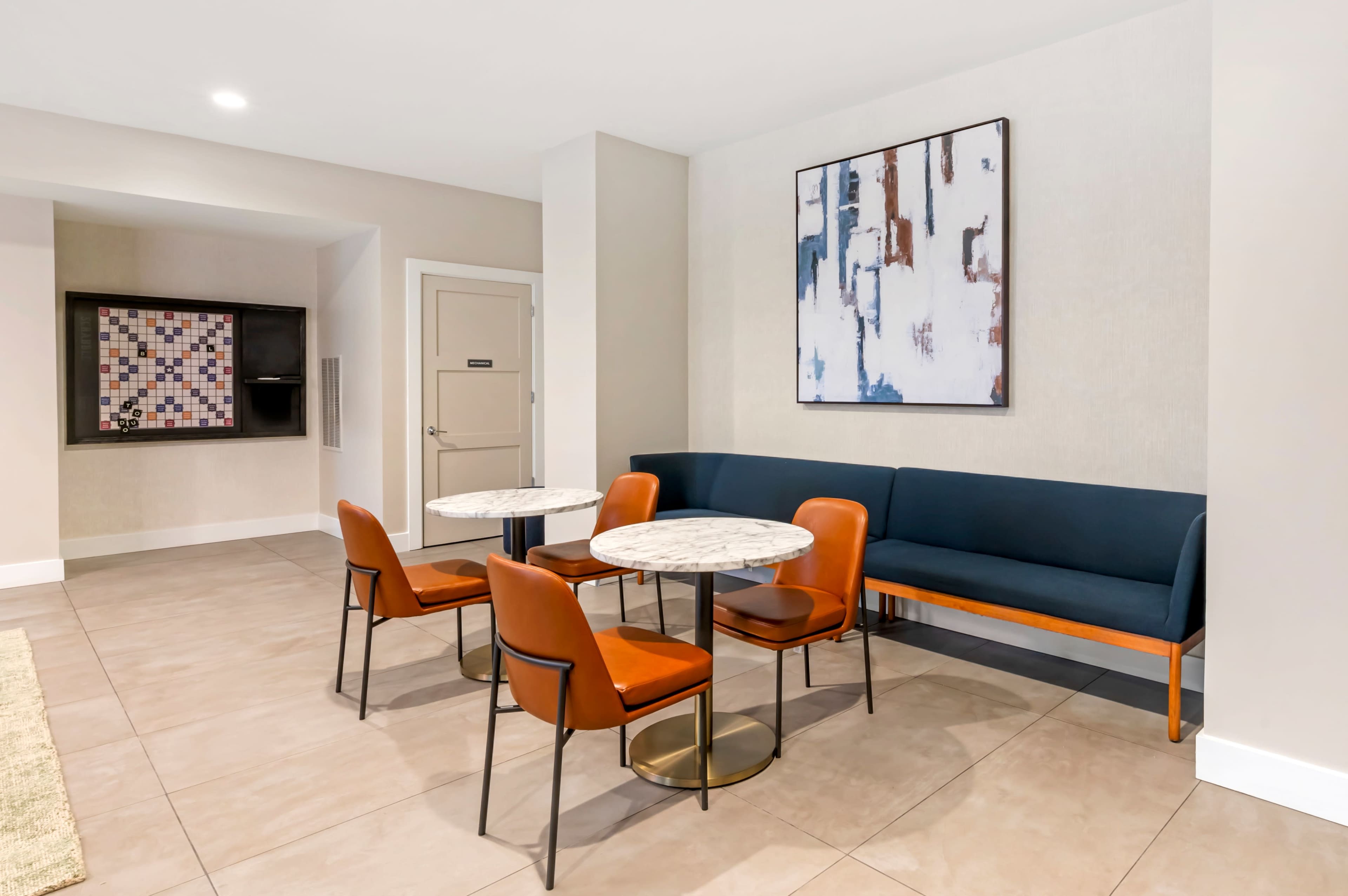 The image shows a modern seating area featuring two marble-top tables surrounded by orange chairs, along with a blue upholstered bench against a beige wall.