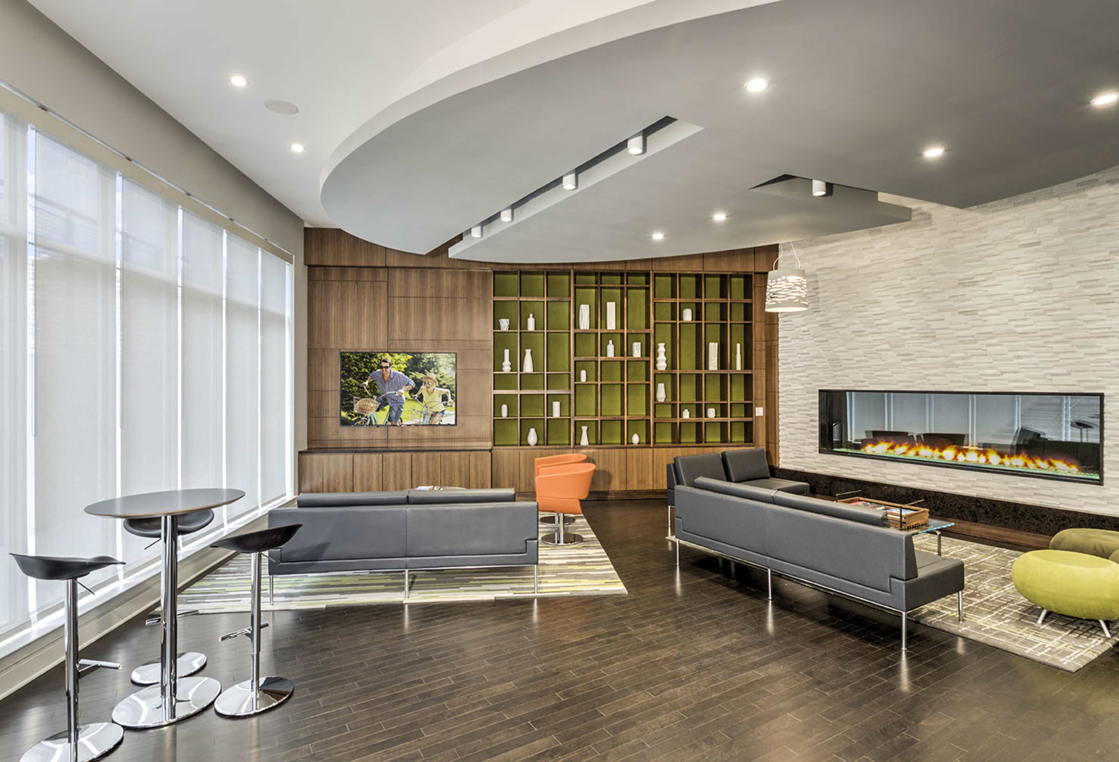 A modern lounge area featuring a sleek fireplace, contemporary furniture, and a green bookshelf backdrop.