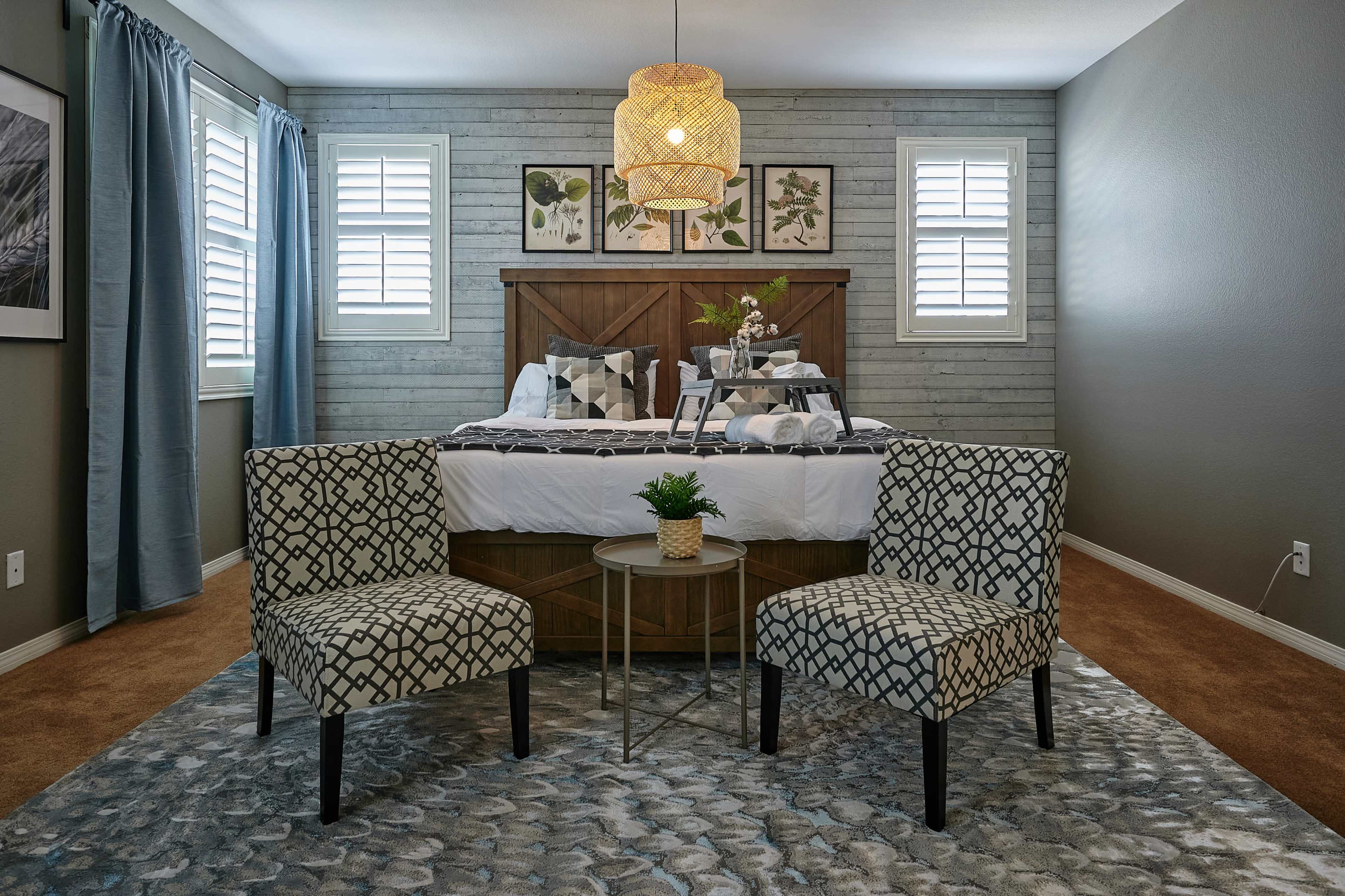A cozy bedroom features a wooden bed against a textured wall, flanked by two patterned chairs and a small round table.