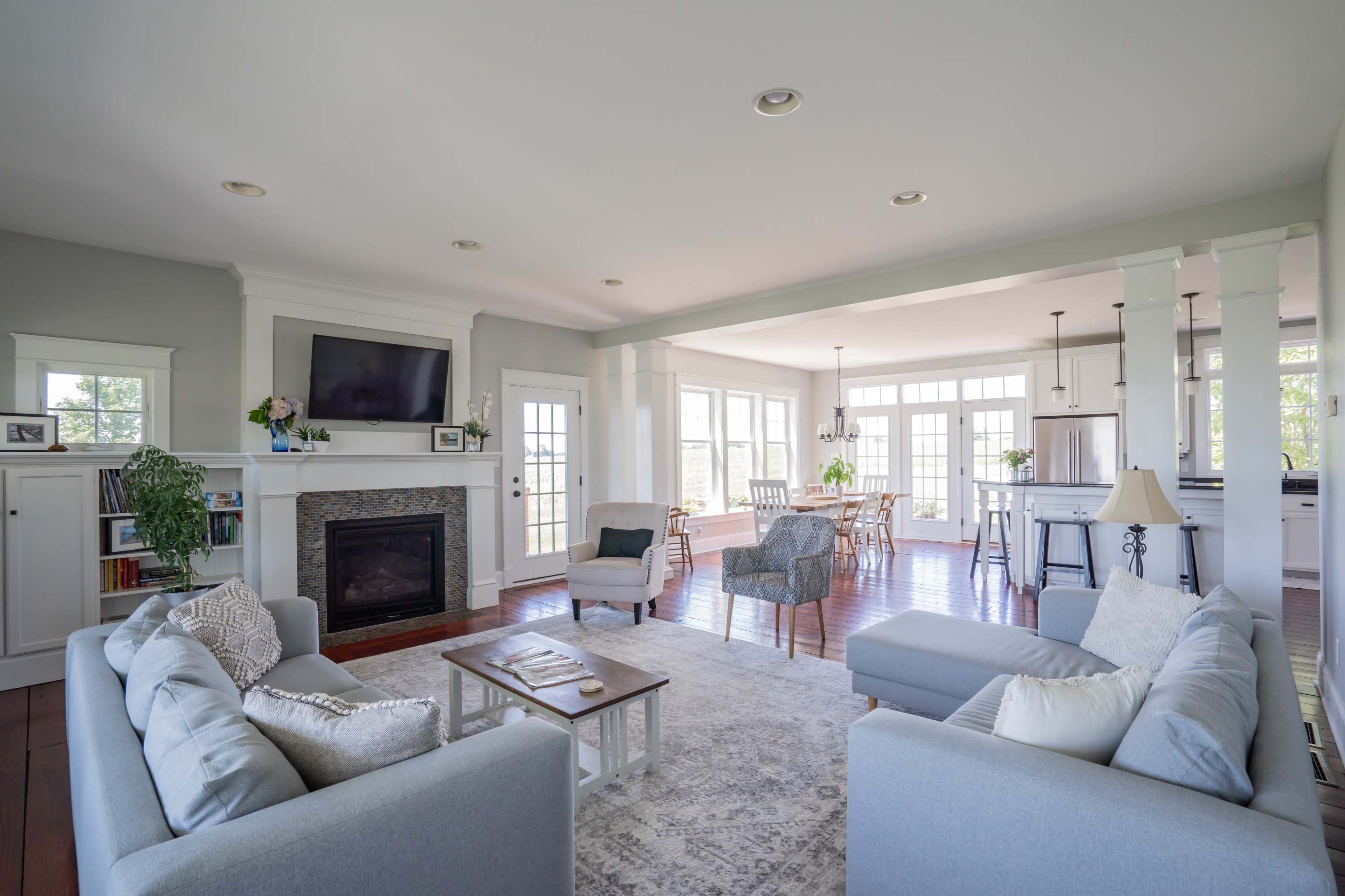 A modern living room with a fireplace, two sofas, and large windows allowing natural light to fill the space.
