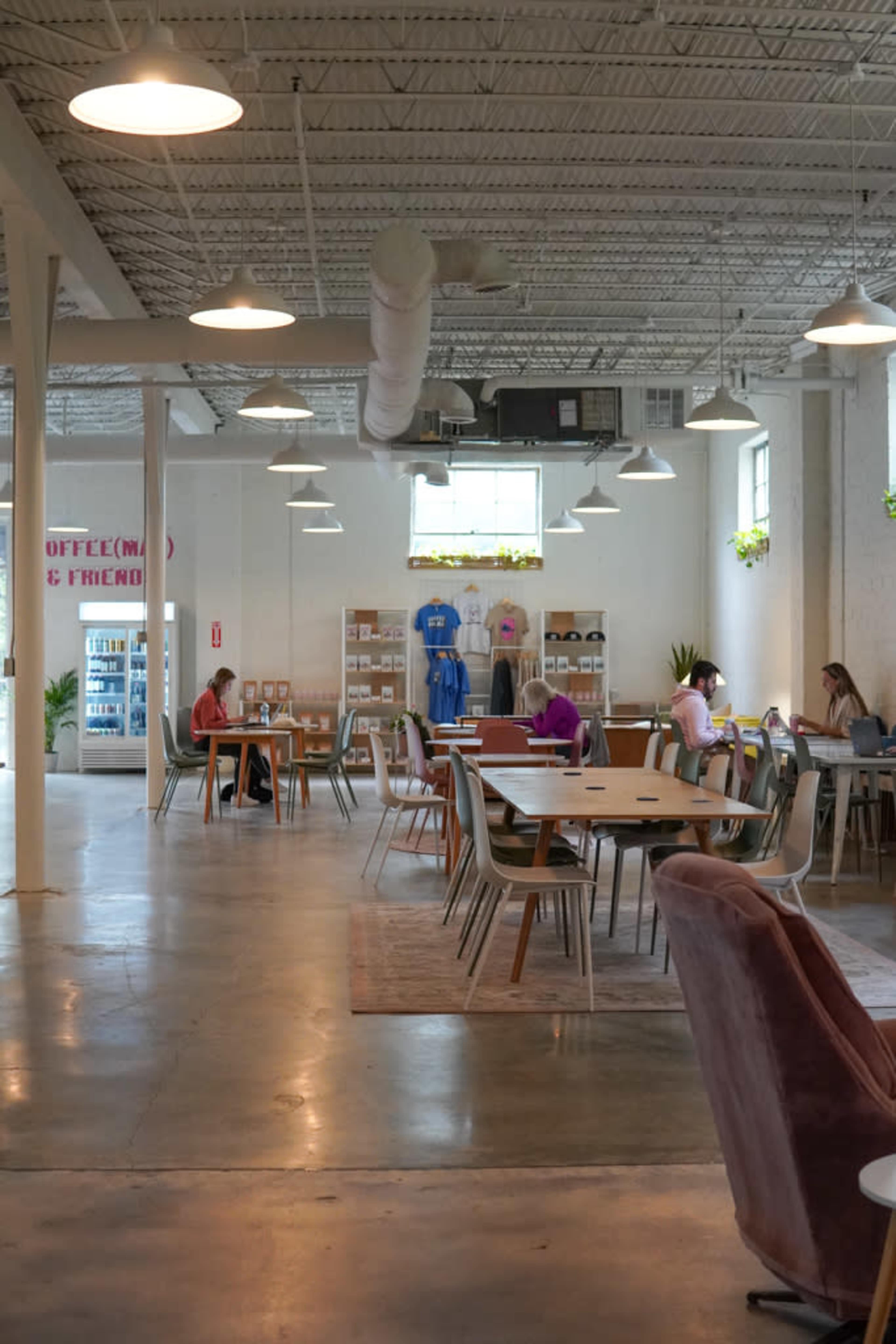 A spacious and well-lit coffee shop with various tables, people working, and merchandise displayed on shelves.