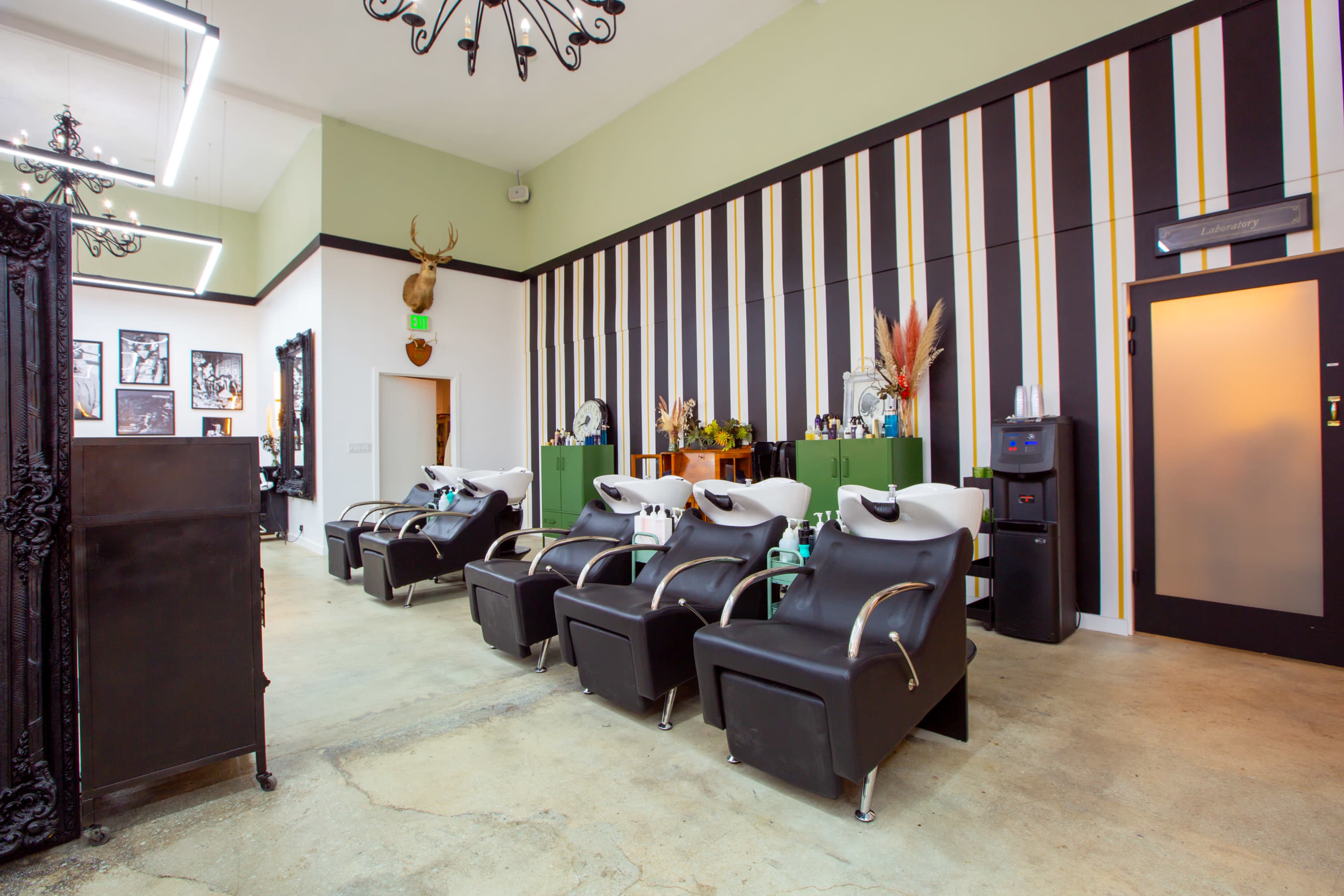 A modern salon interior with black and green styling chairs arranged in front of a striped wall and decorative accents.