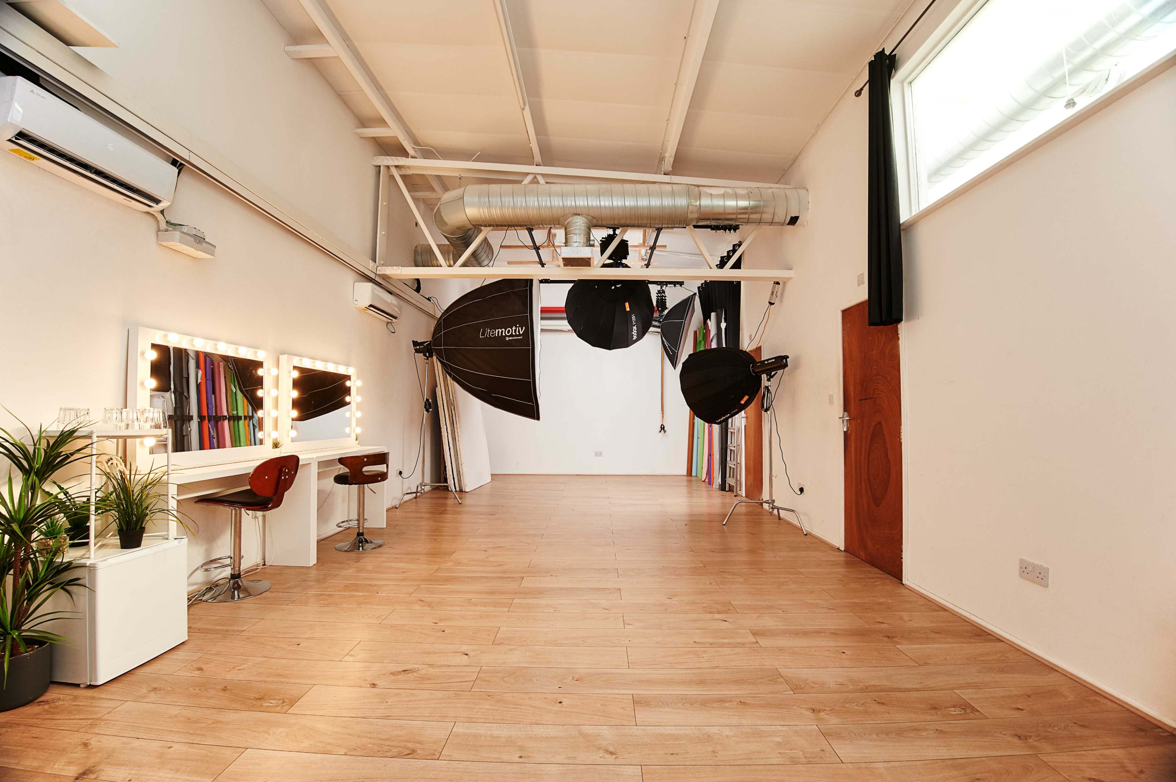 A spacious photography studio with large backdrop rolls, professional lighting equipment, and a makeup vanity area.