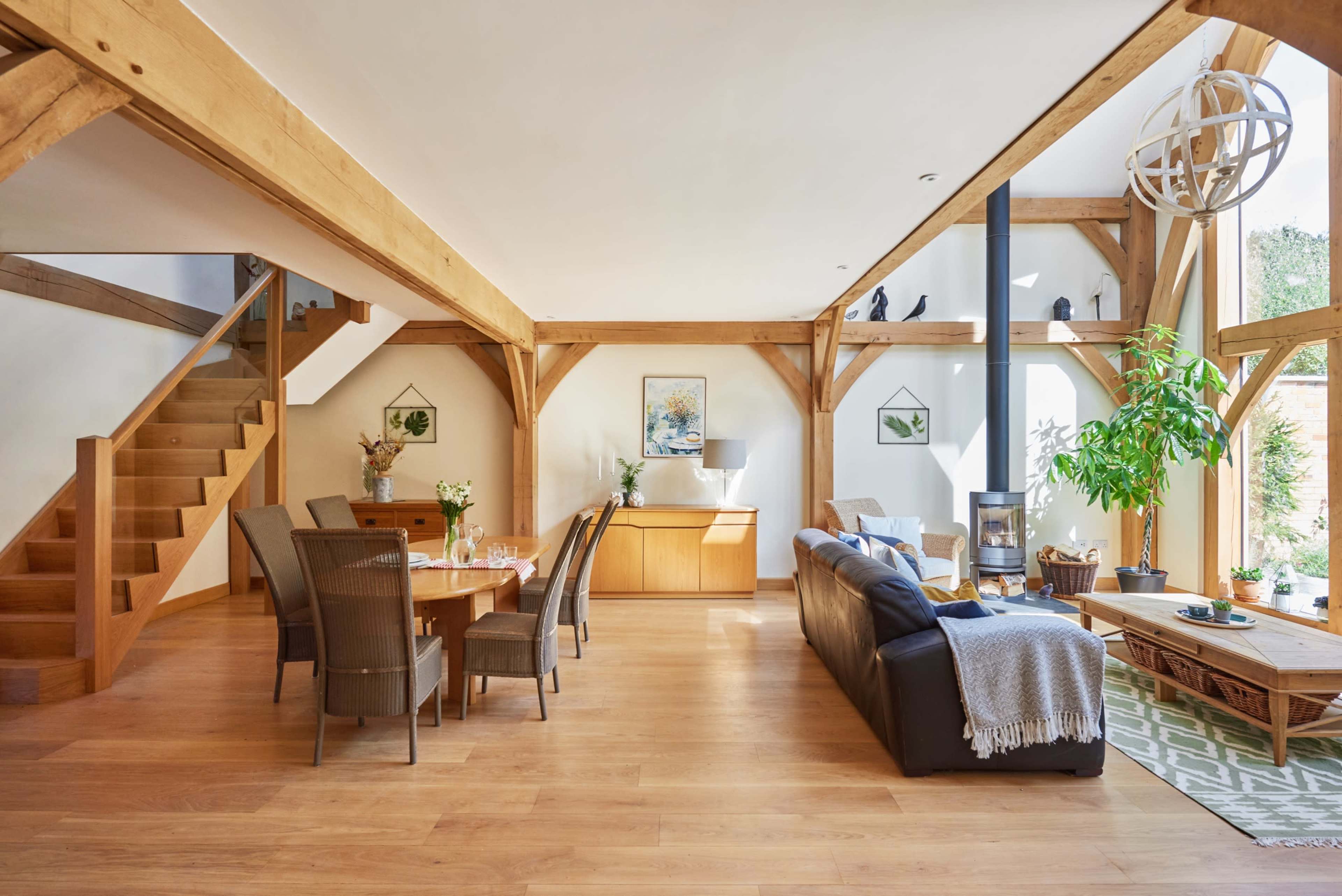 A modern living space with wooden beams, a dining area with a table and chairs, a seating area with a sofa, and a staircase leading to an upper level.