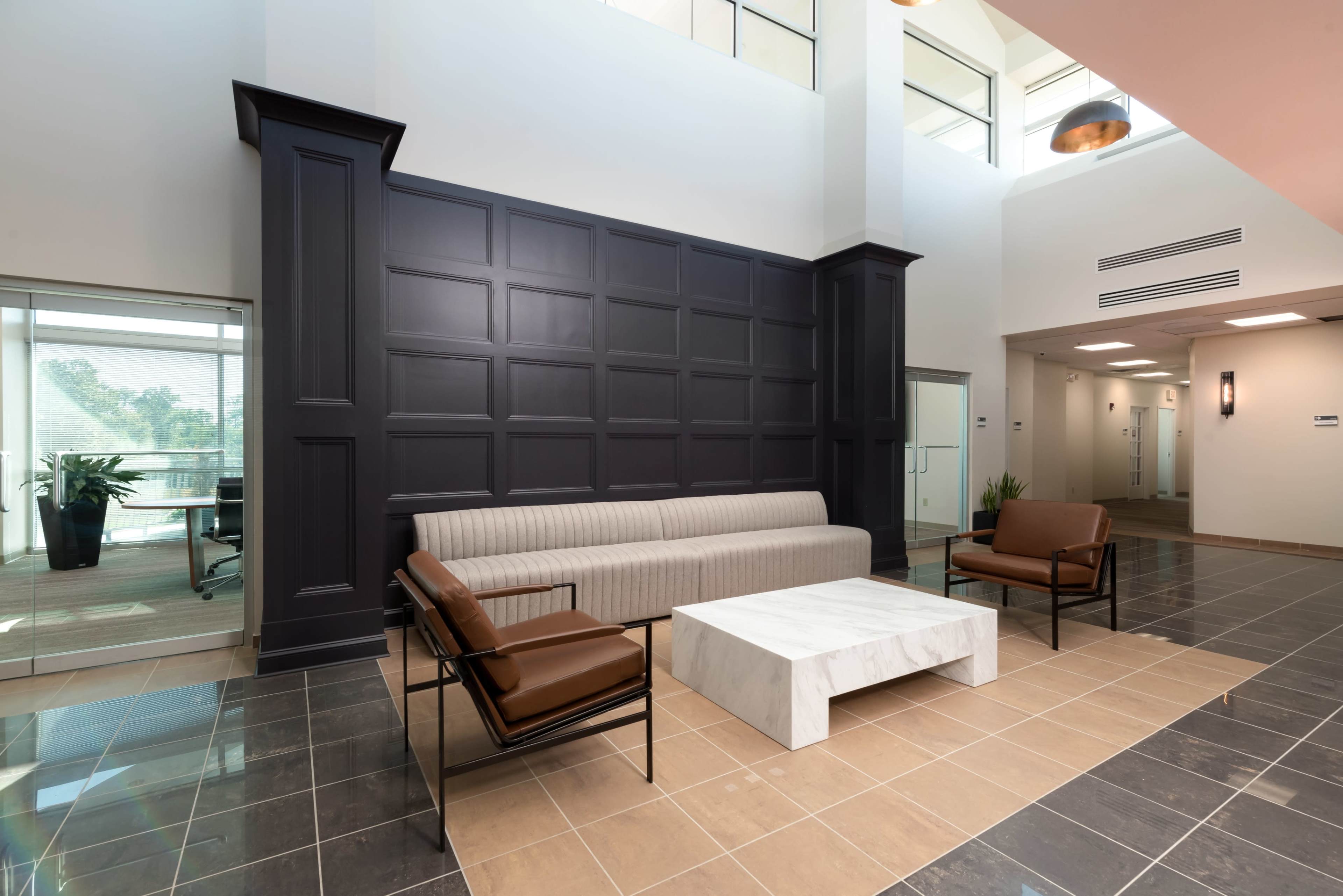 A modern lobby area with a striped sofa, two brown chairs, and a marble coffee table, complemented by a dark-paneled wall.