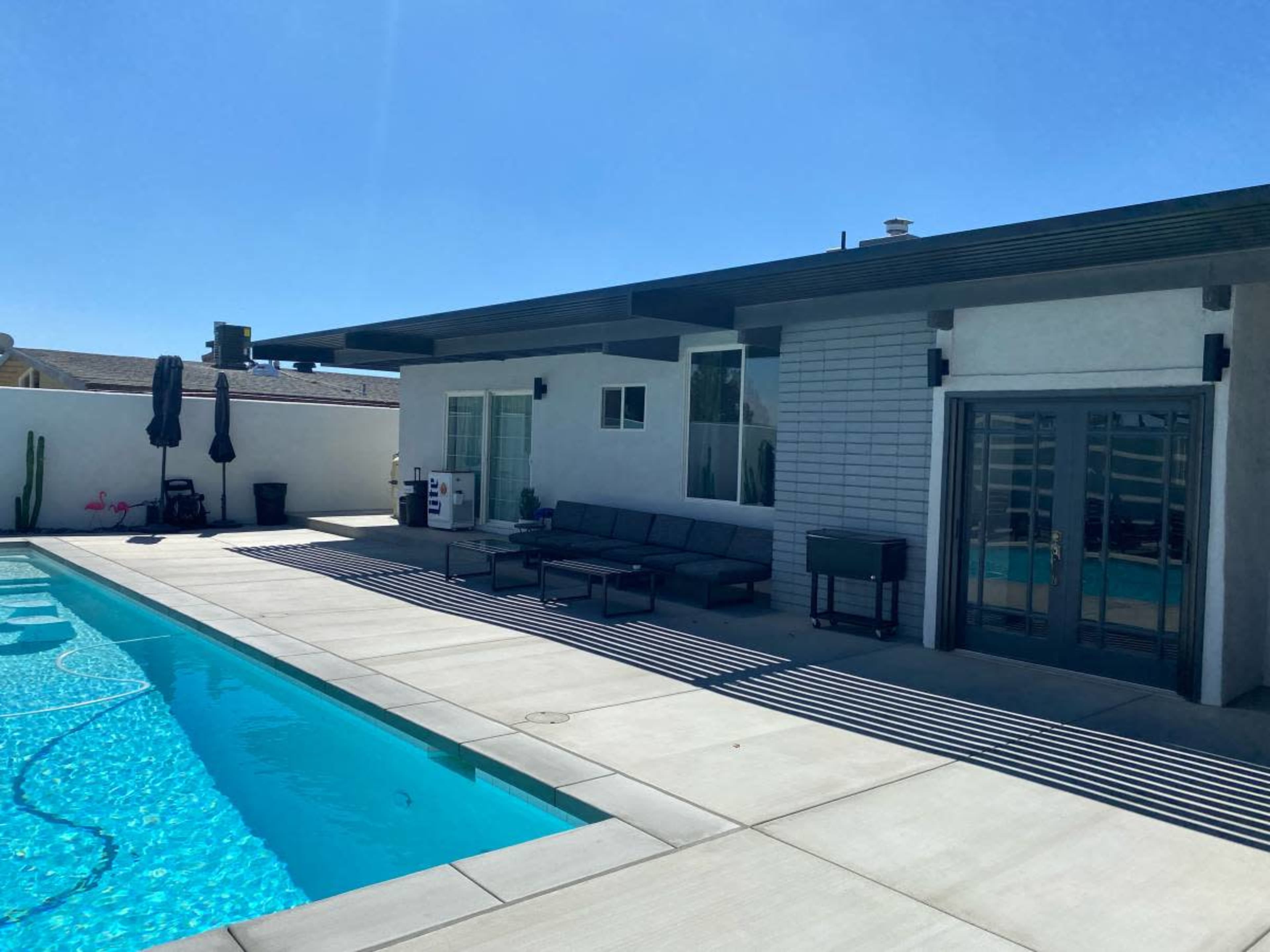 A modern house with a spacious patio and a swimming pool is shown under clear blue skies.