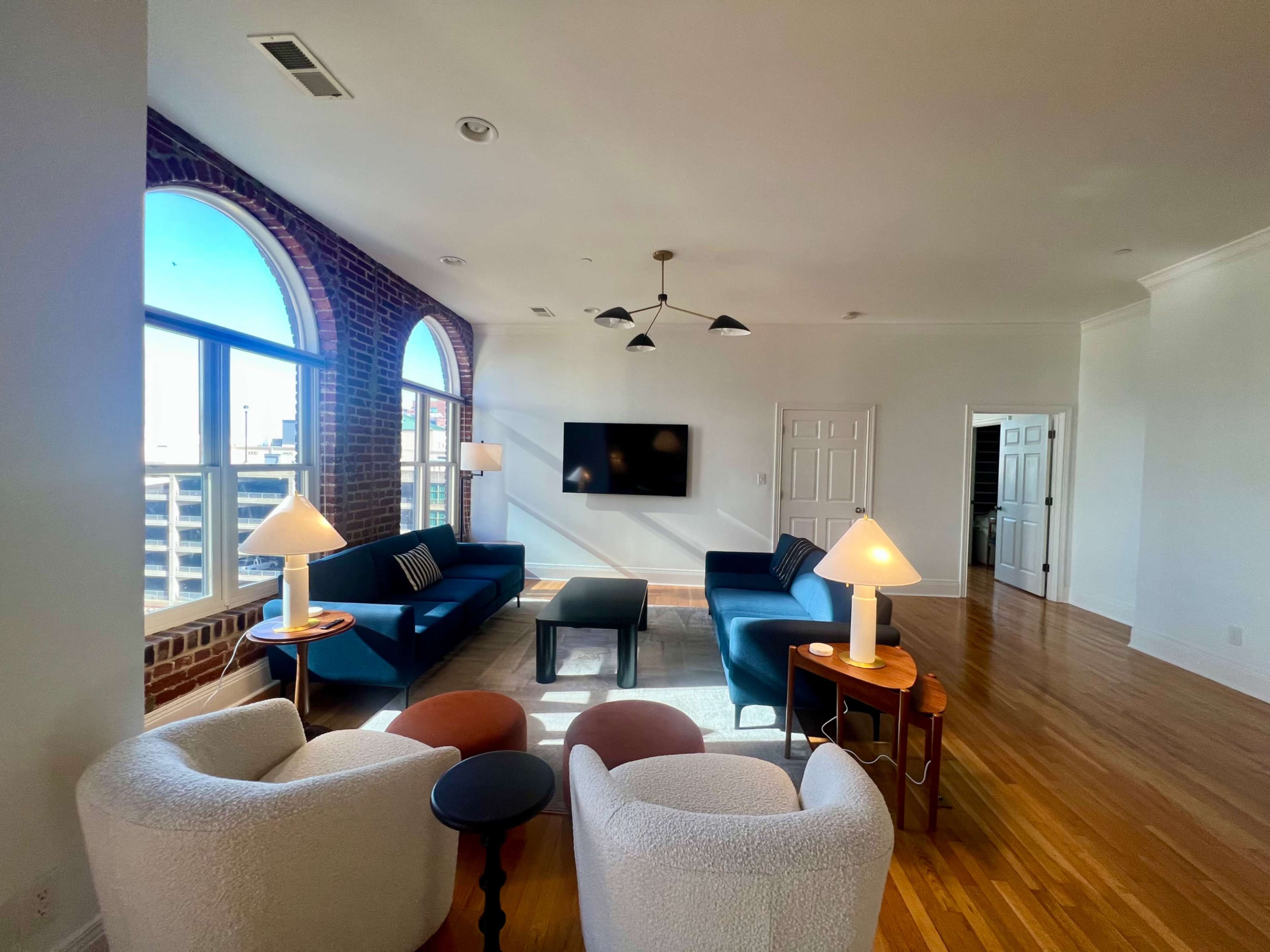 A modern living room with large arched windows, two blue sofas, a small coffee table, and two accent chairs beside lamps.