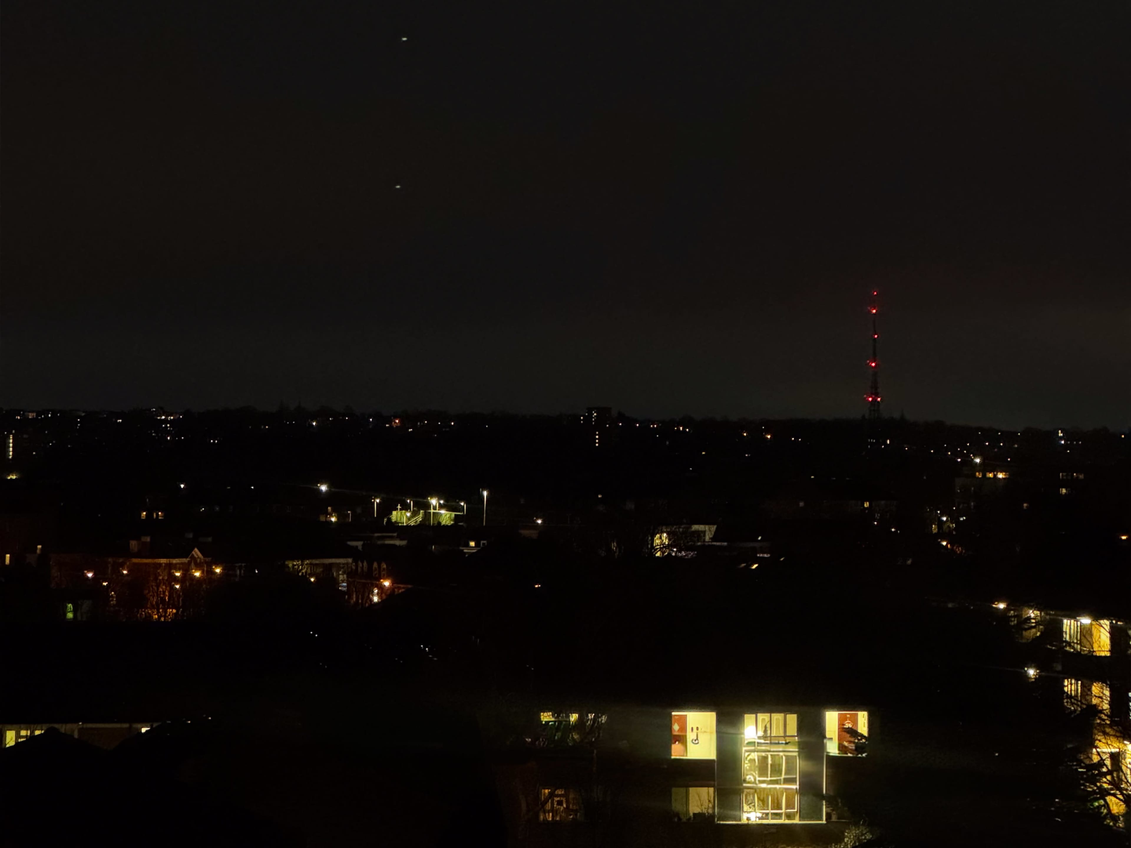 The image shows a city skyline at night, illuminated by various lights, with a transmission tower visible in the background.