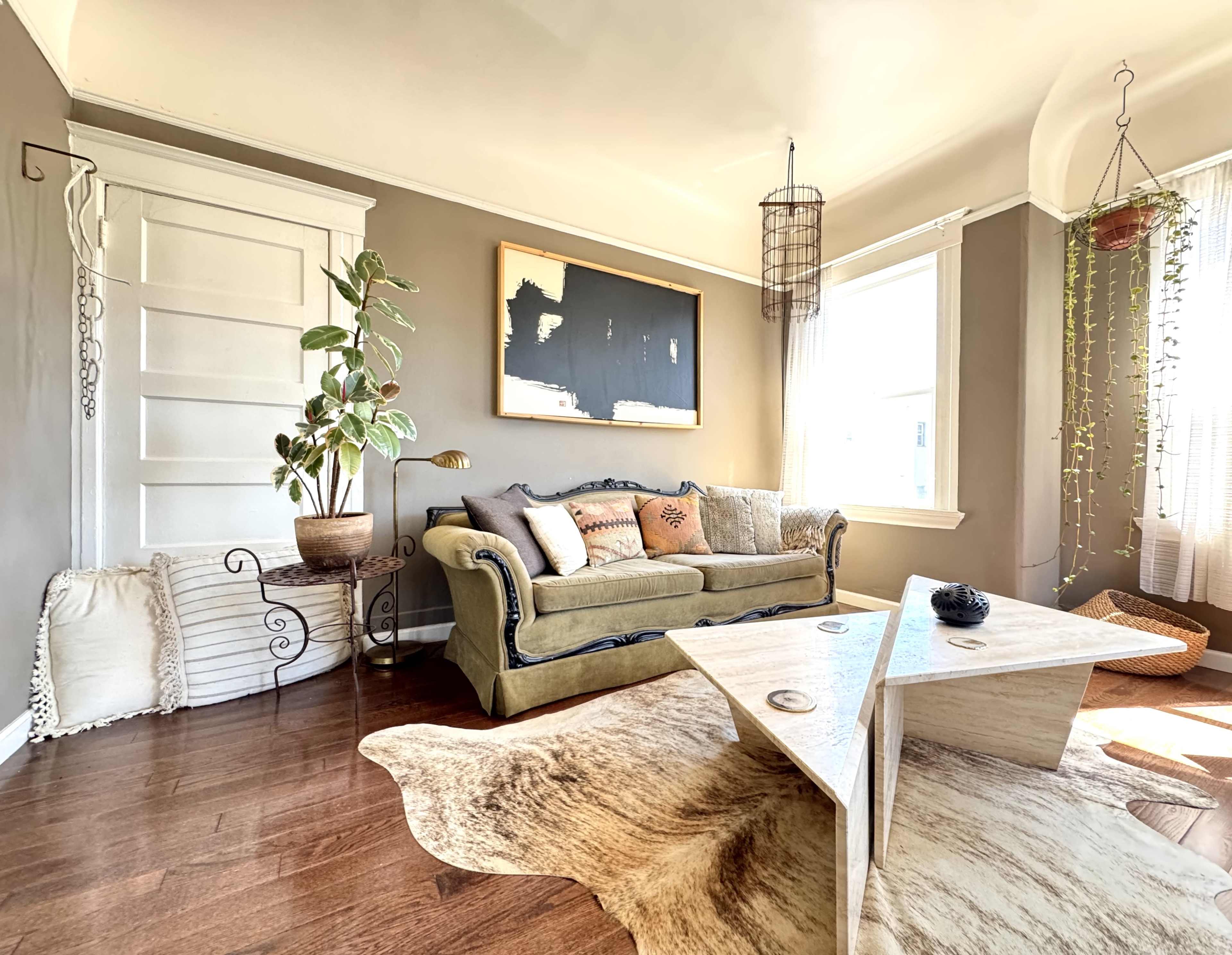 A cozy living room features a green sofa, a coffee table made of light wood, and plants near large windows.