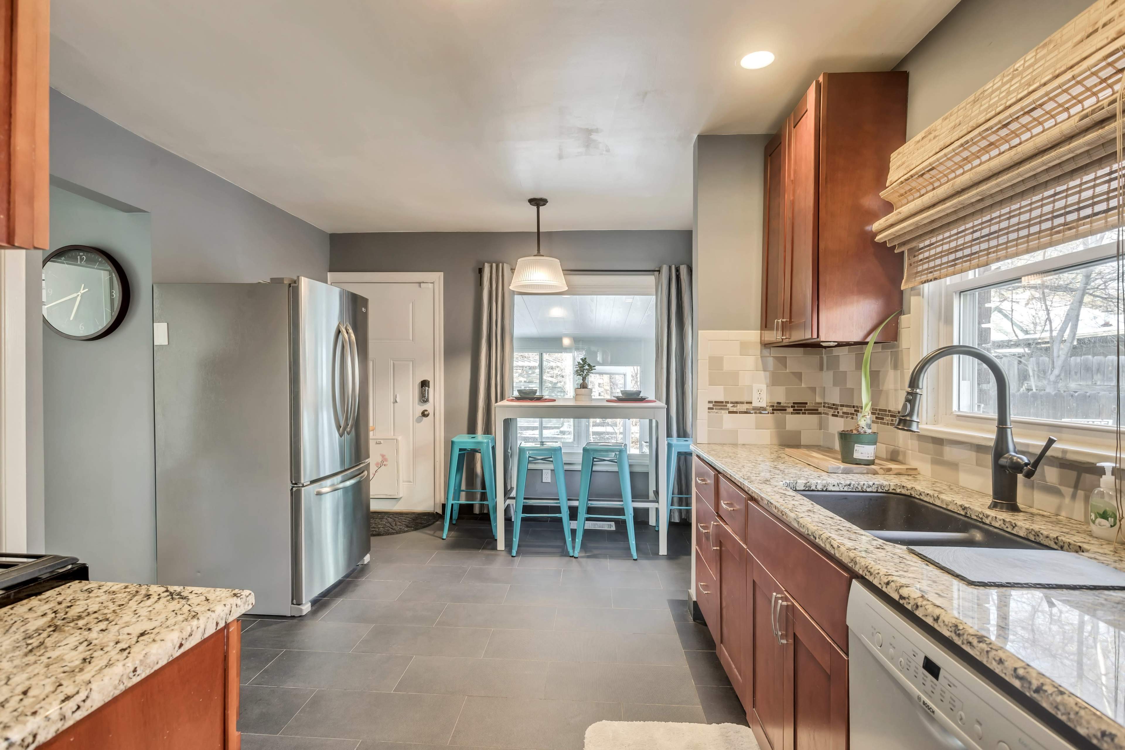 A modern kitchen featuring wooden cabinets, stainless steel appliances, and a small dining area with teal stools.