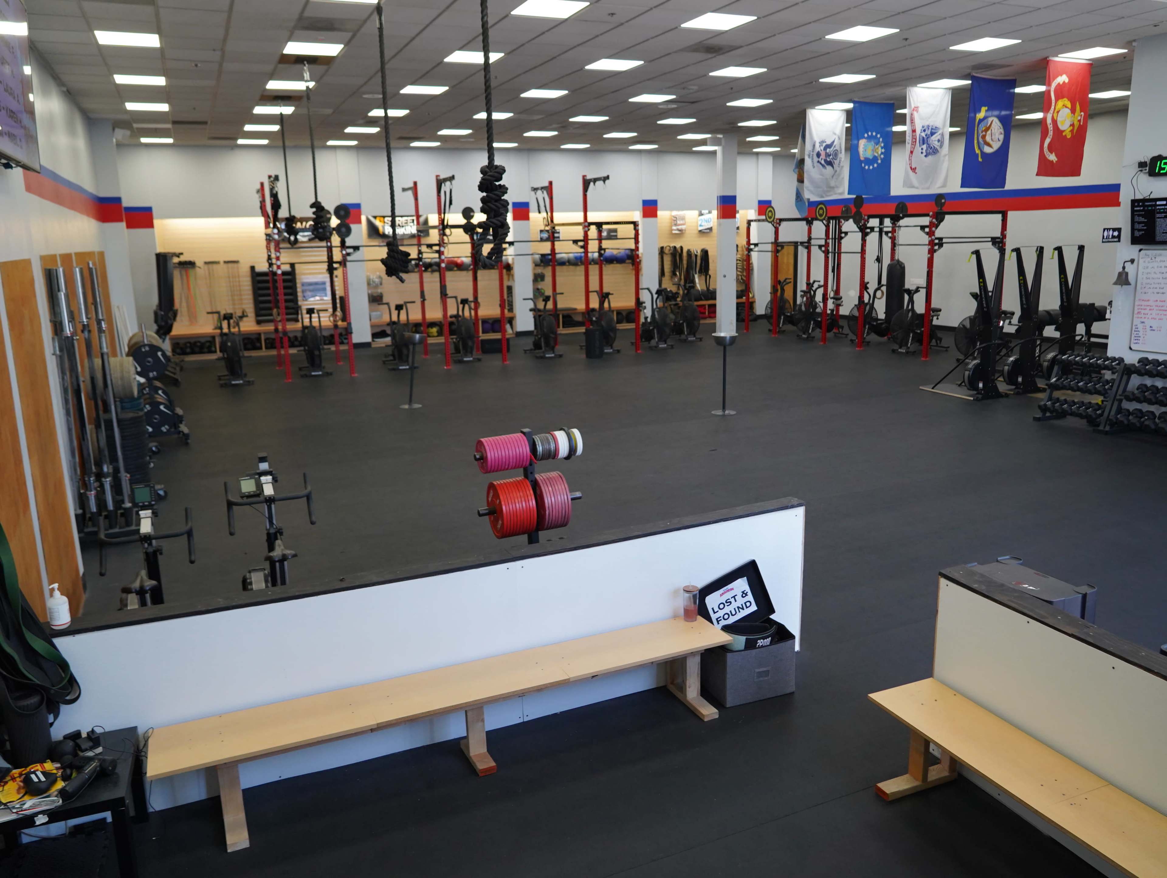 The image shows a spacious gym interior with various workout equipment, including free weights and resistance machines, set up in organized sections.