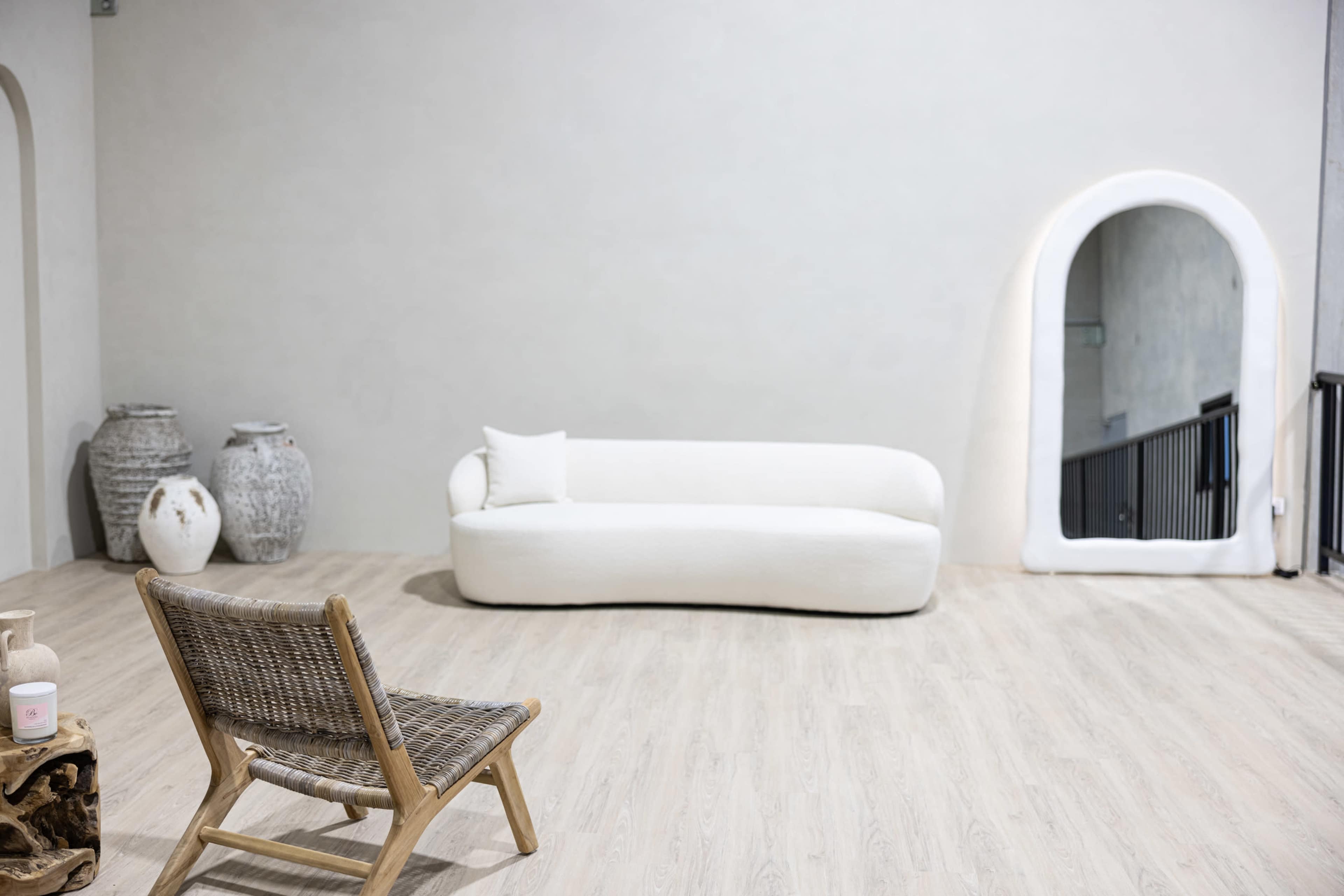 The scene features a minimalist room with a white curvy sofa, a wooden chair, and decorative vases against a light-colored wall.