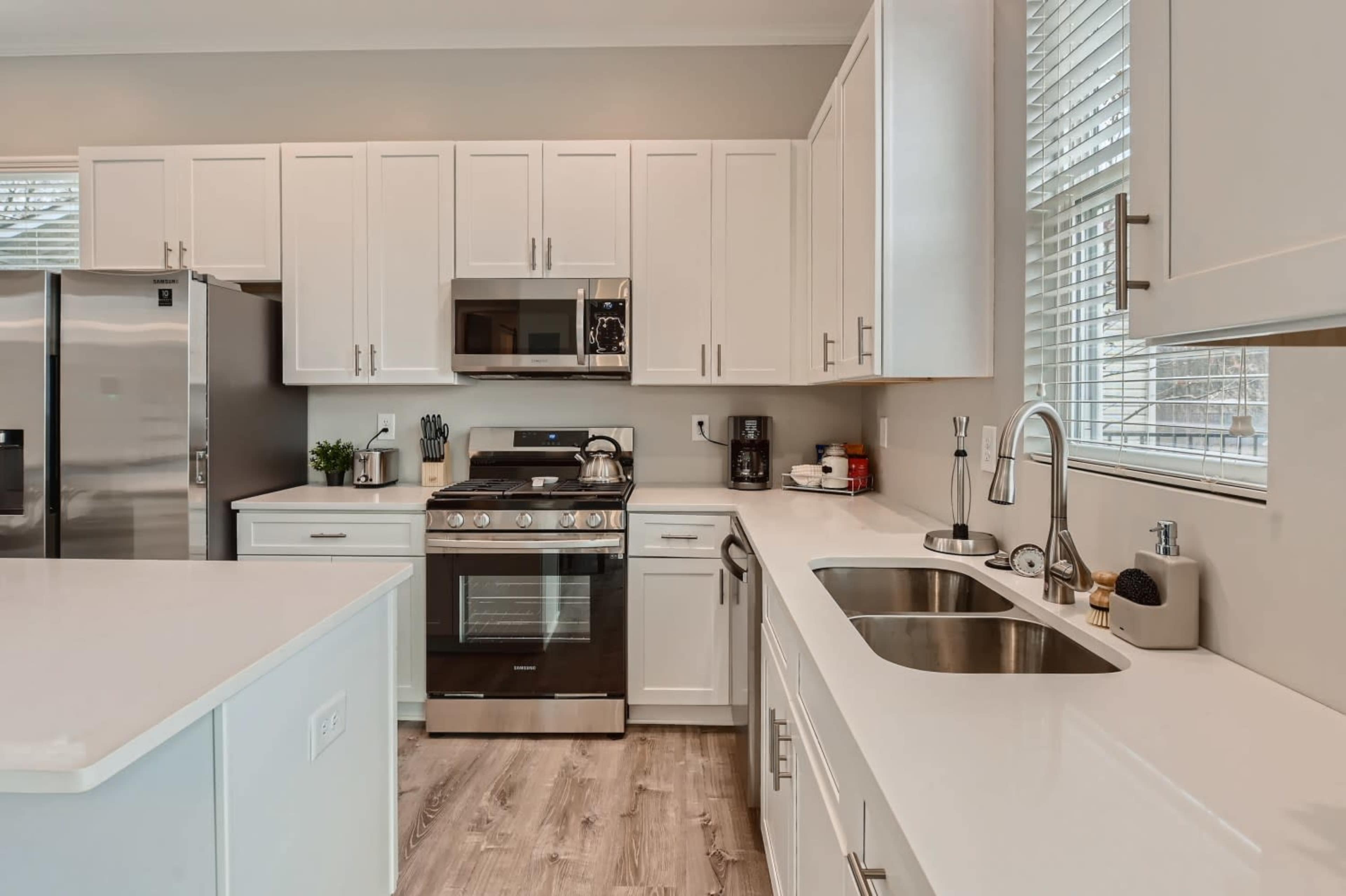 A modern kitchen features white cabinetry, stainless steel appliances, and a central island with a sink.