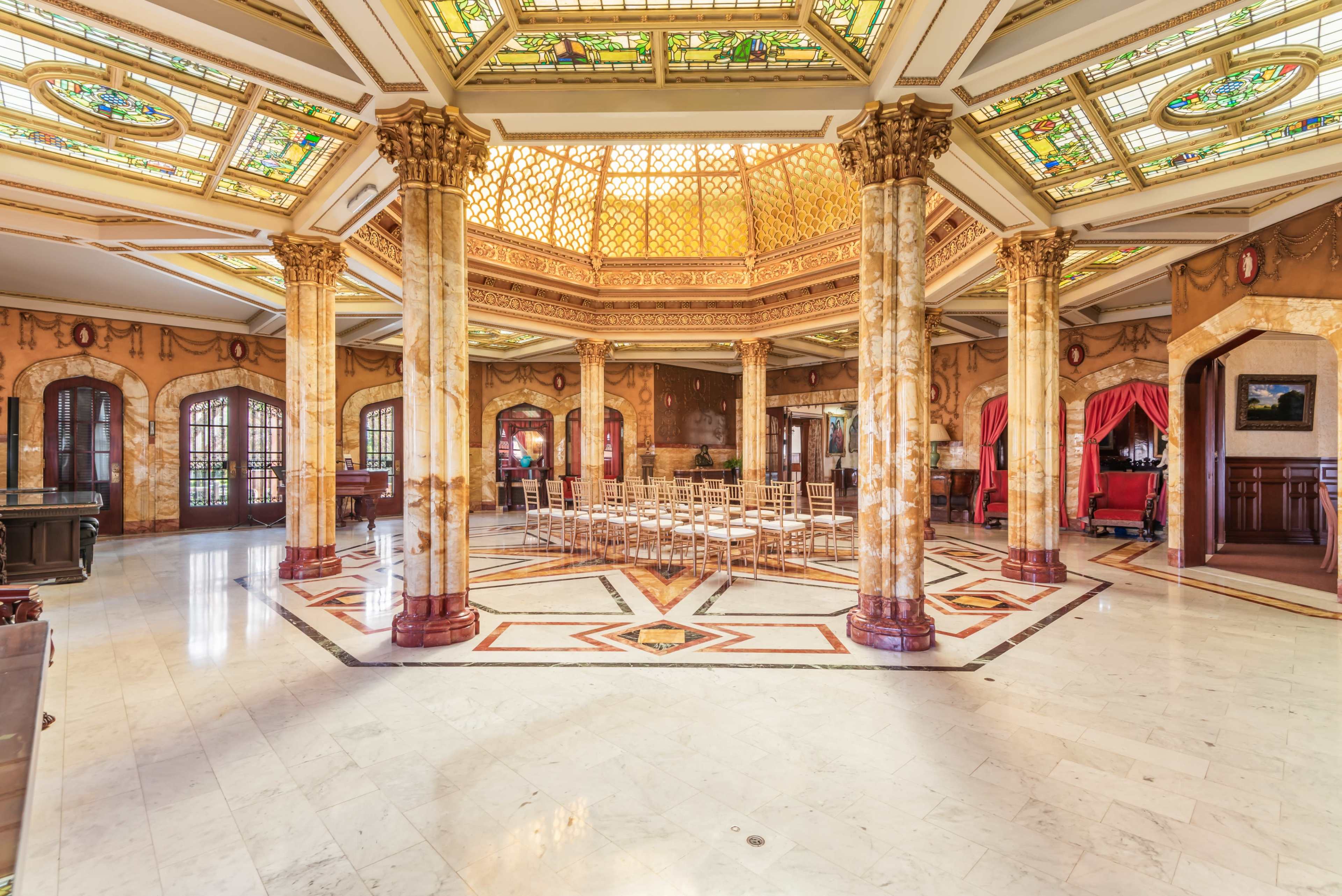 The image shows a grand, ornate interior space with marble floors, decorative columns, and stained glass windows.