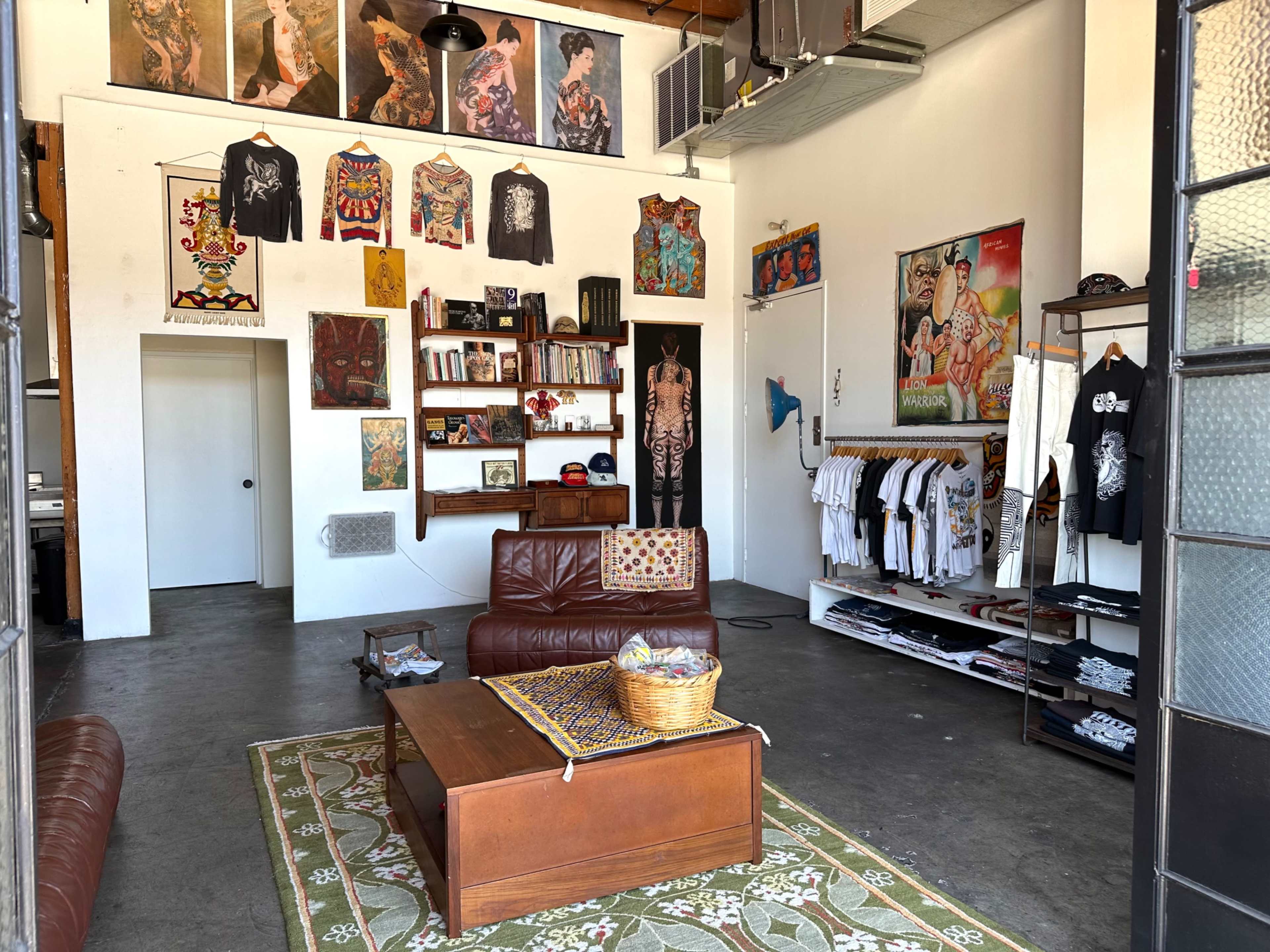 The image shows a boutique interior with various artworks and clothing displayed on the walls and racks, featuring a leather sofa and a coffee table in the center.