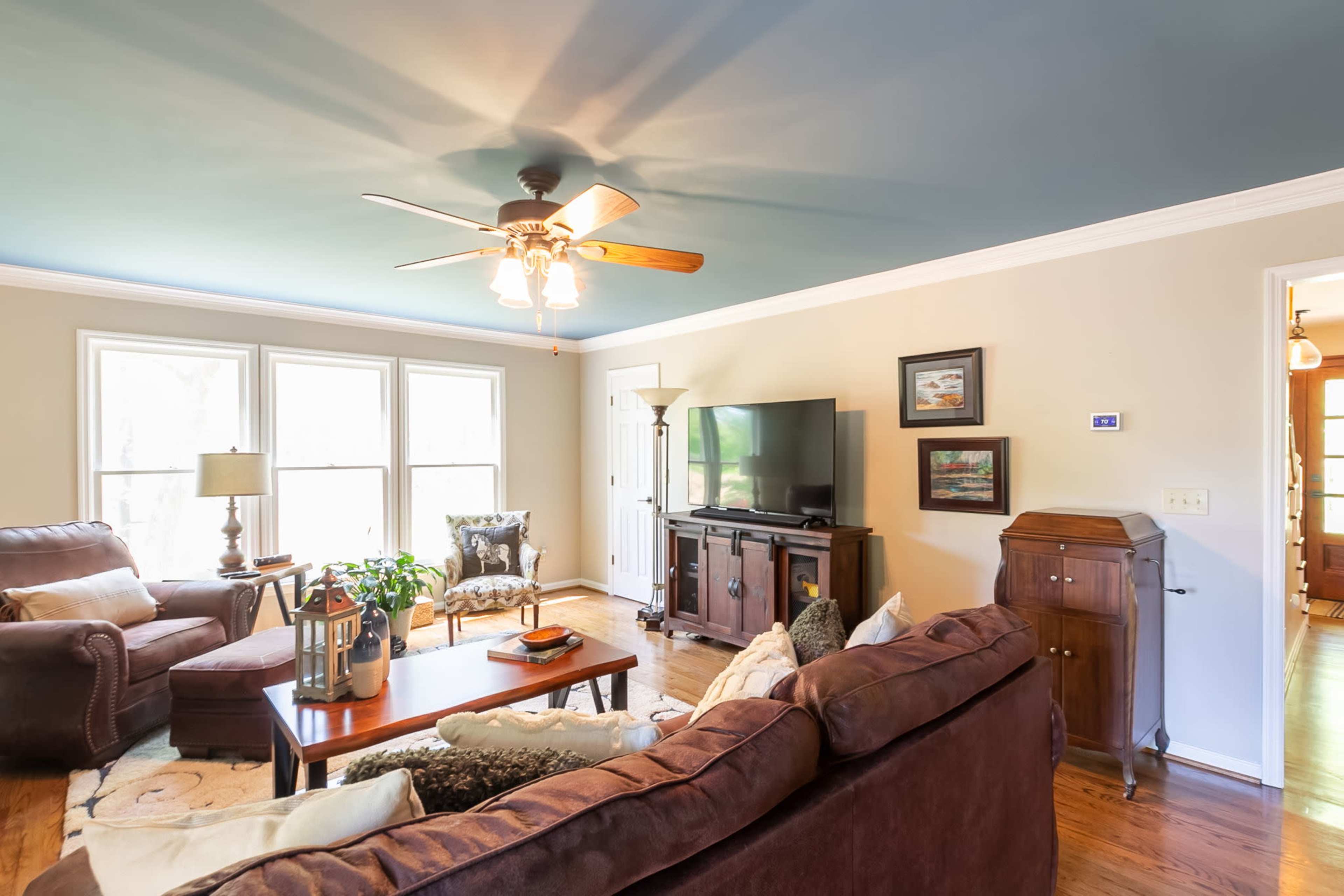 The living room features two large windows, a ceiling fan, a television cabinet, and comfortable seating arranged around a wooden coffee table.