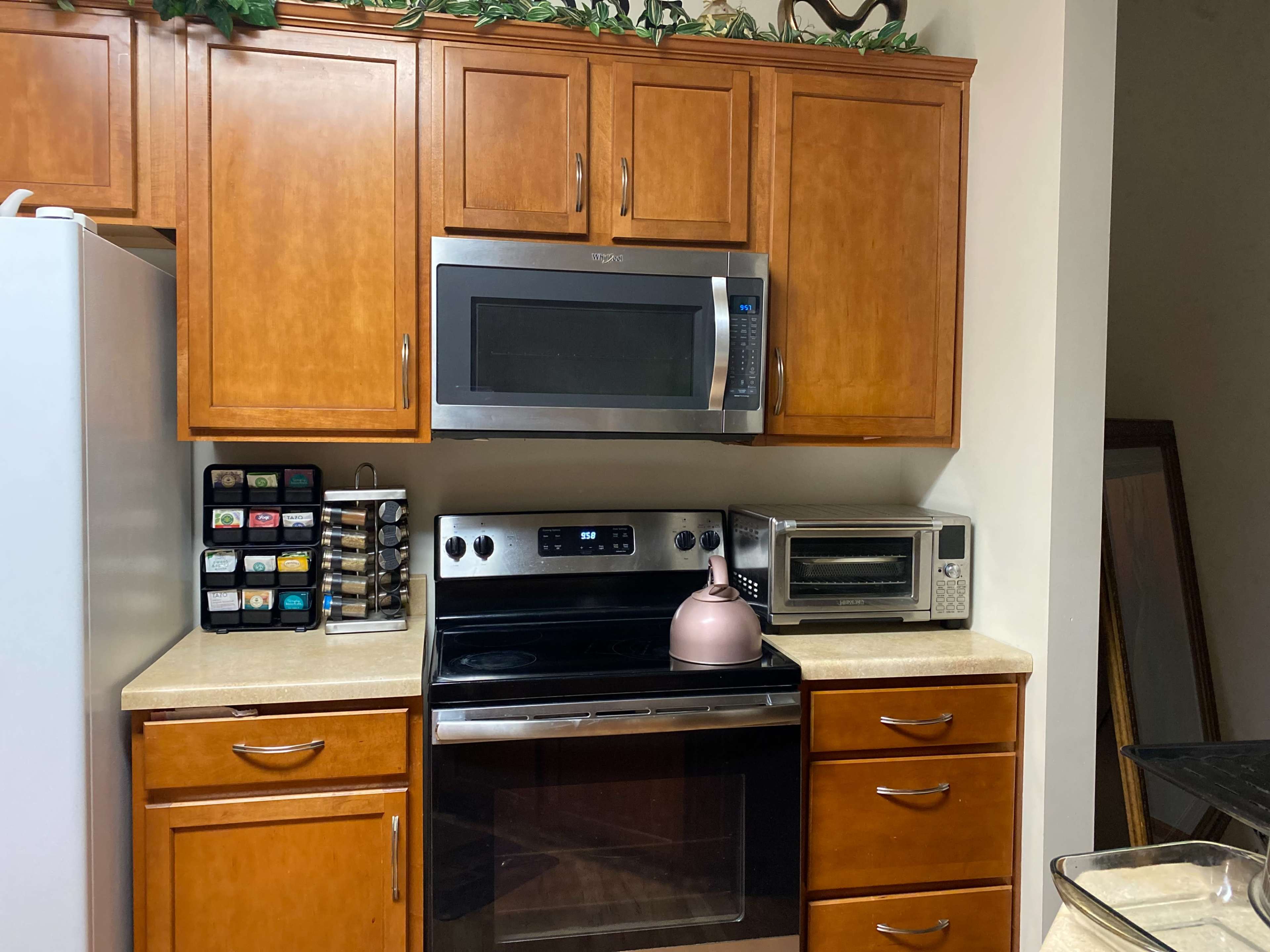 A kitchen with wooden cabinets, a microwave, an oven, an electric kettle, and a countertop appliance.