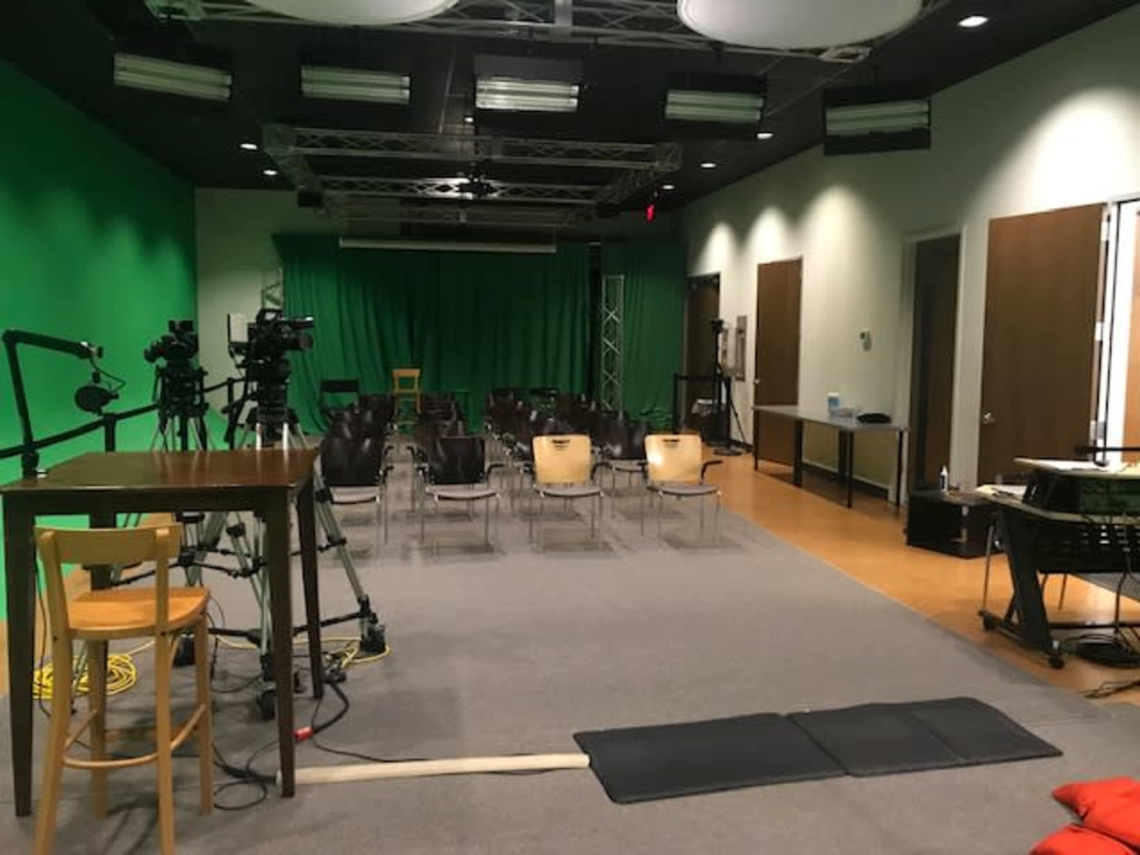 A film studio with a green screen backdrop, empty chairs arranged in rows, and various cameras and equipment set up for recording.