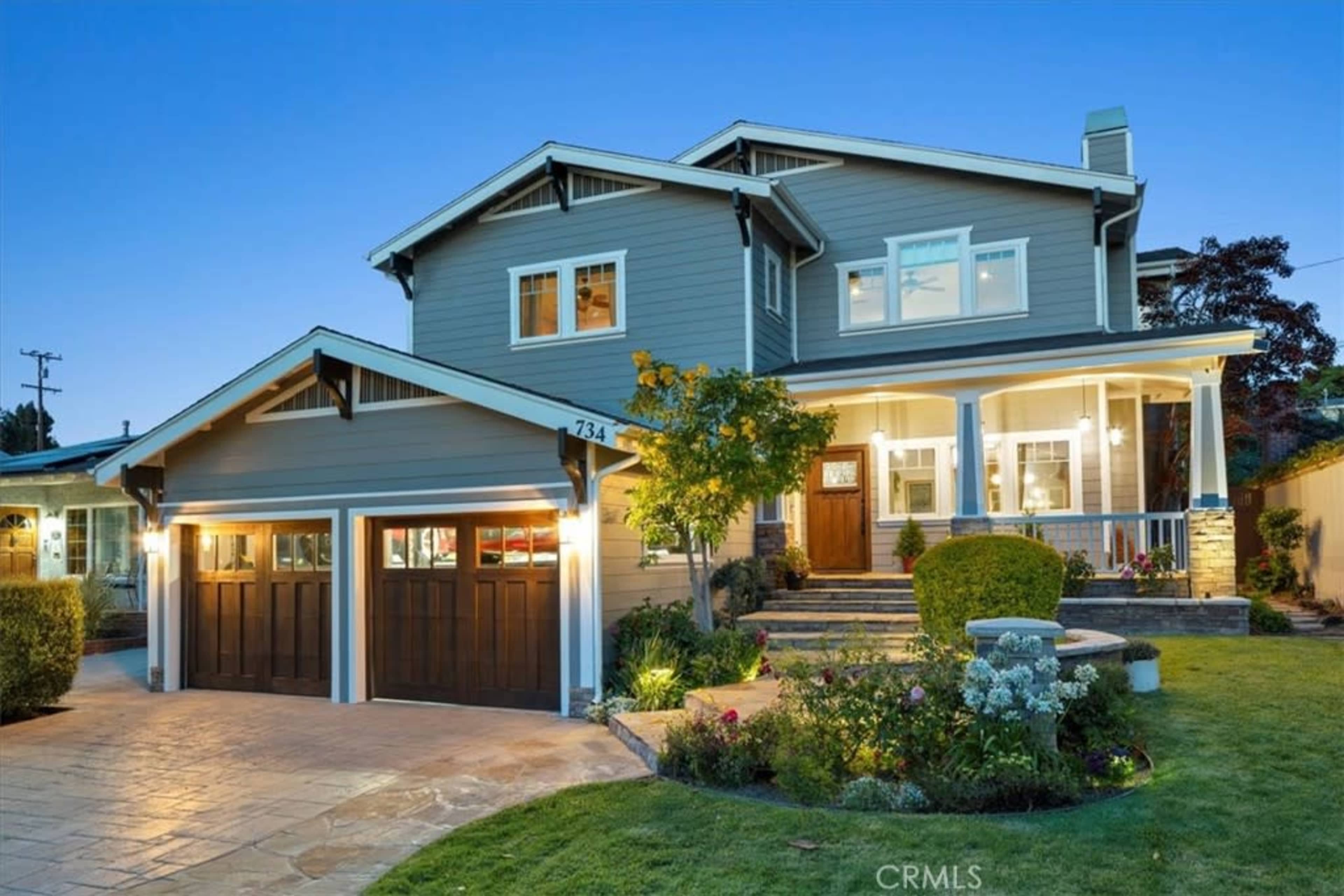 A two-story house with a front porch and manicured landscaping is illuminated at dusk.