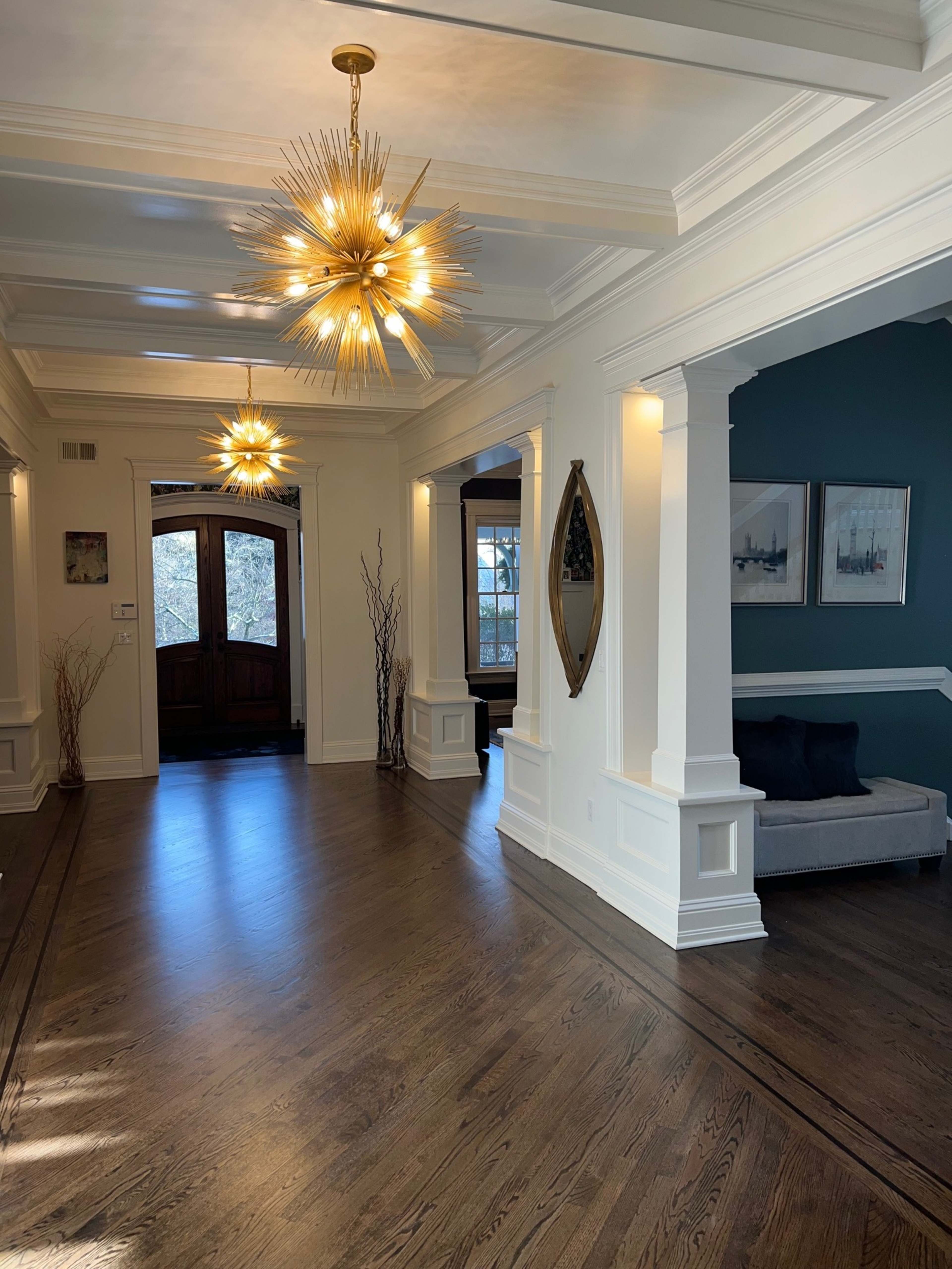 The image shows a spacious hallway with decorative lighting fixtures, wooden floors, and a seating area along one wall.