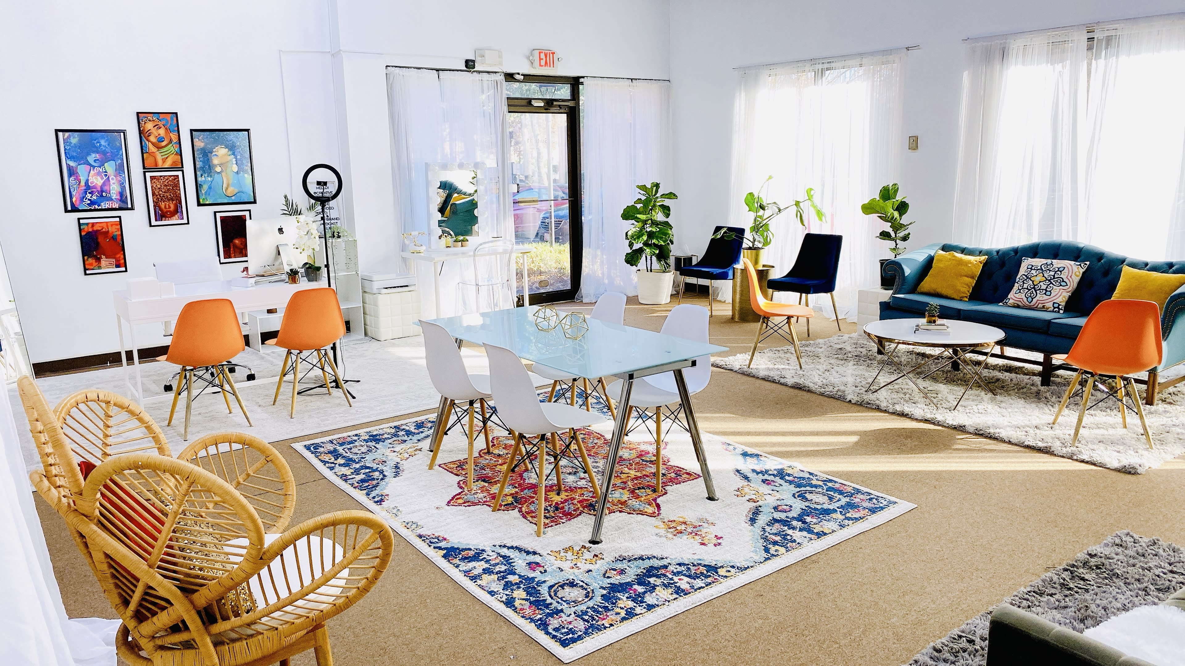 A bright, modern interior space featuring a glass dining table surrounded by white and orange chairs, complemented by a blue sofa and several potted plants.