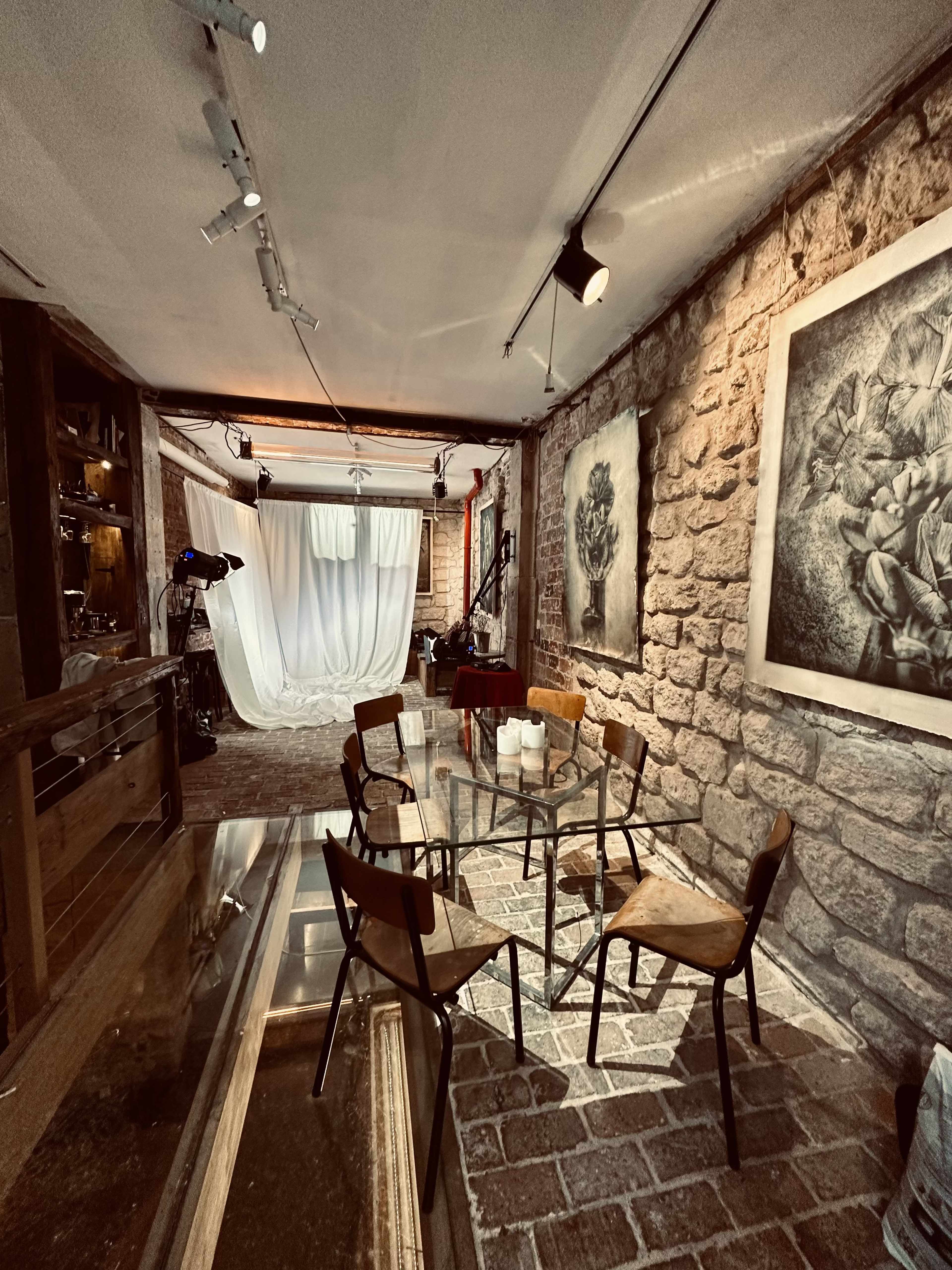 A rustic studio space with exposed stone walls, a small seating area with wooden chairs, and art displayed on the wall.