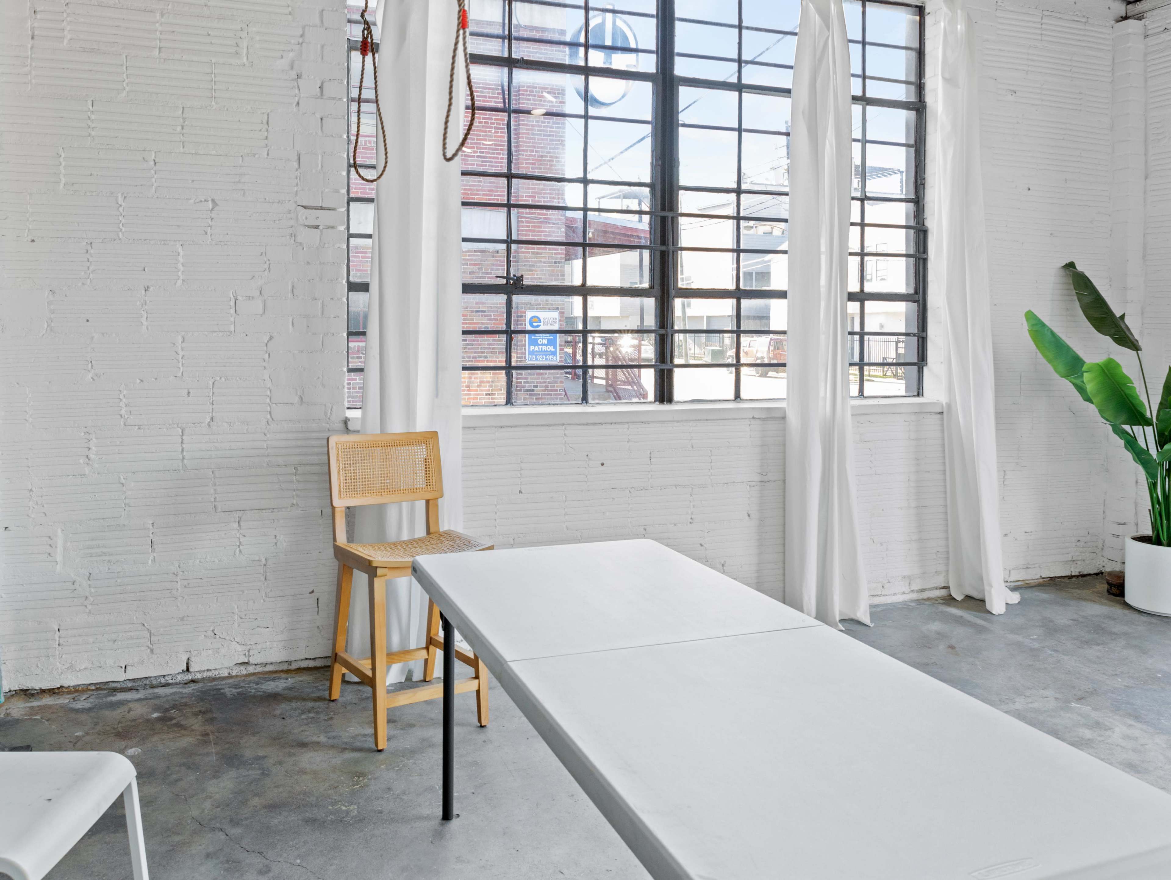 An empty room with a wooden chair and a table near a large window with white curtains.