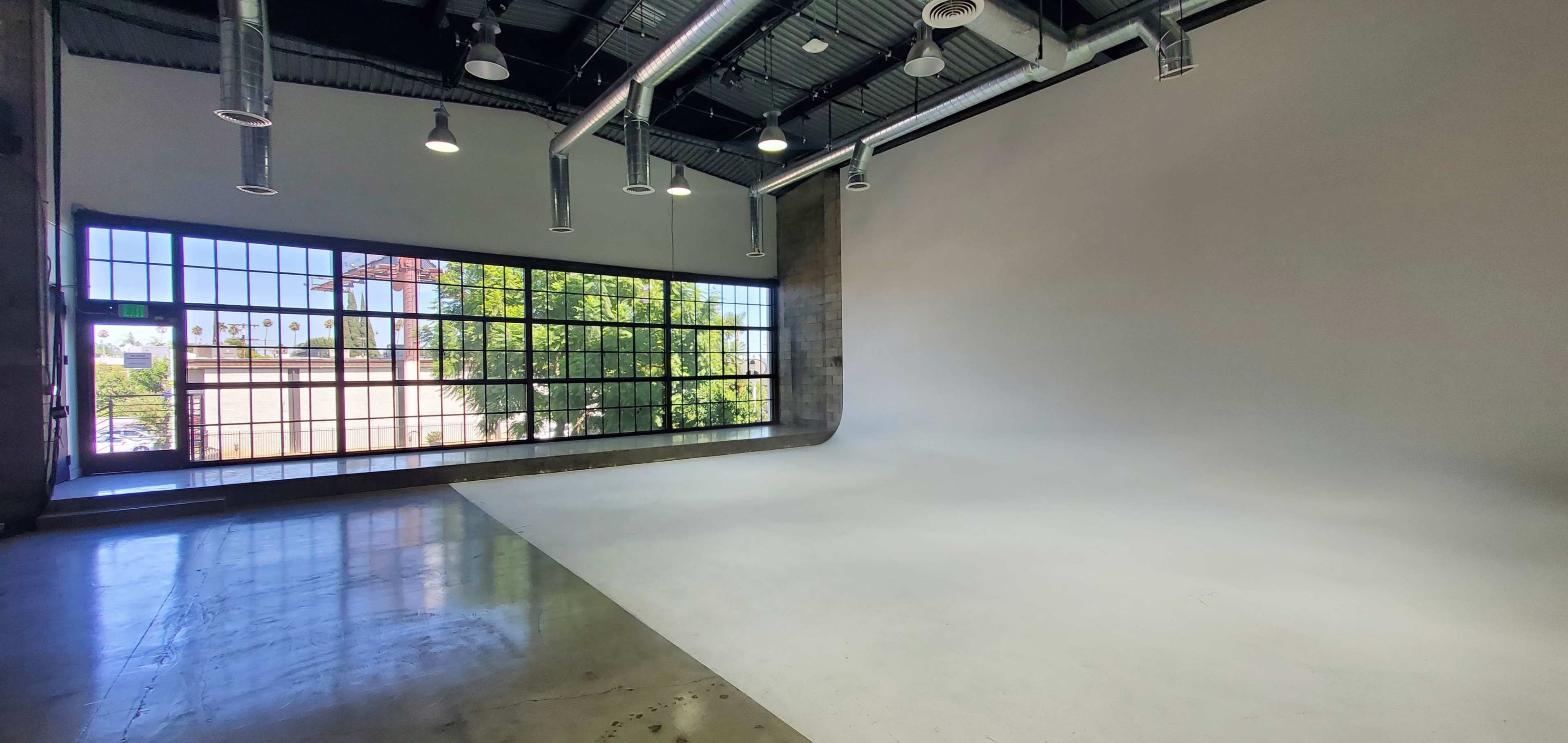 A spacious photography studio with a large window and a plain white backdrop.