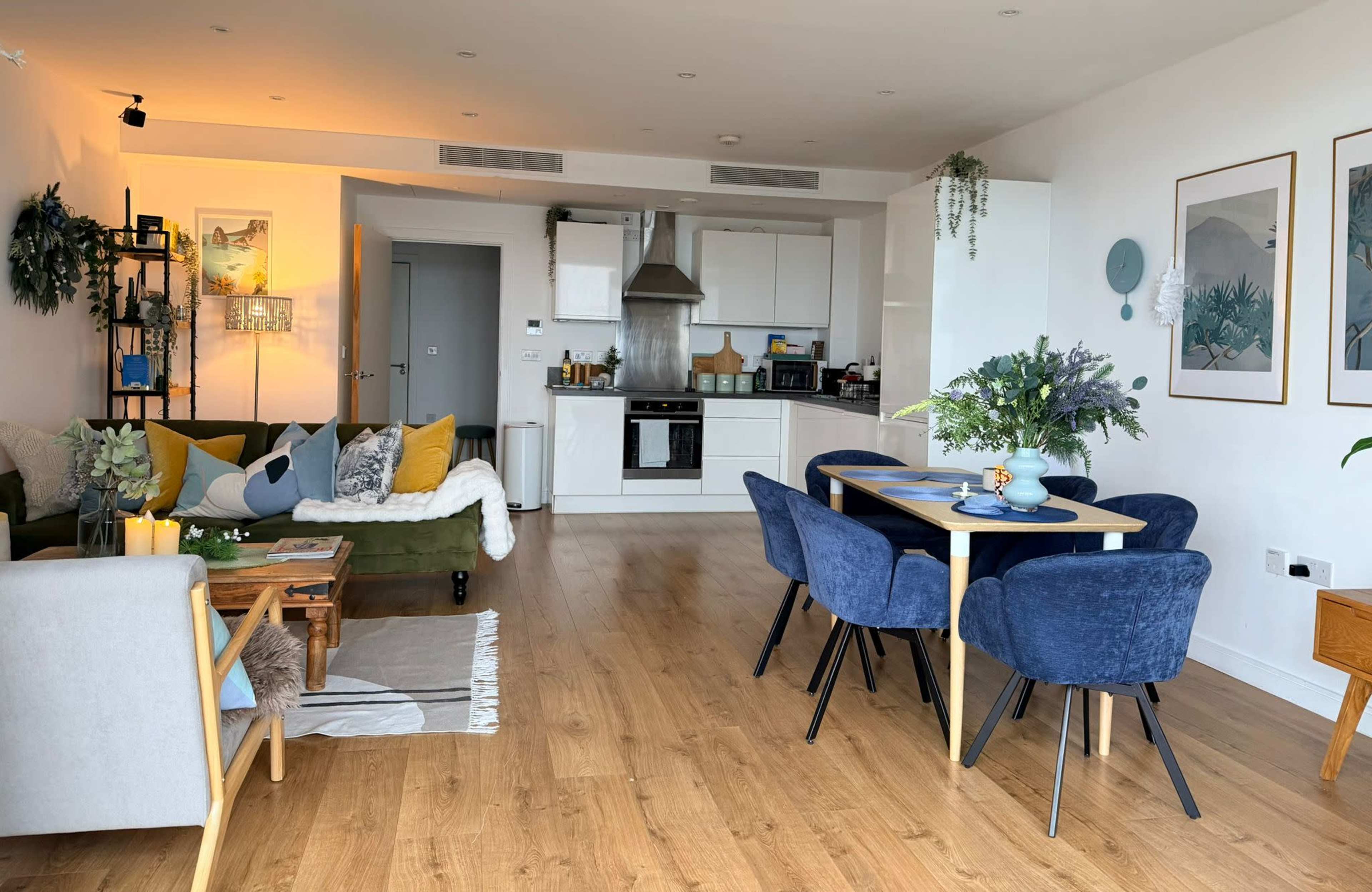The image shows a modern living space with a green sofa, dining table, and a kitchen in a bright, open layout.