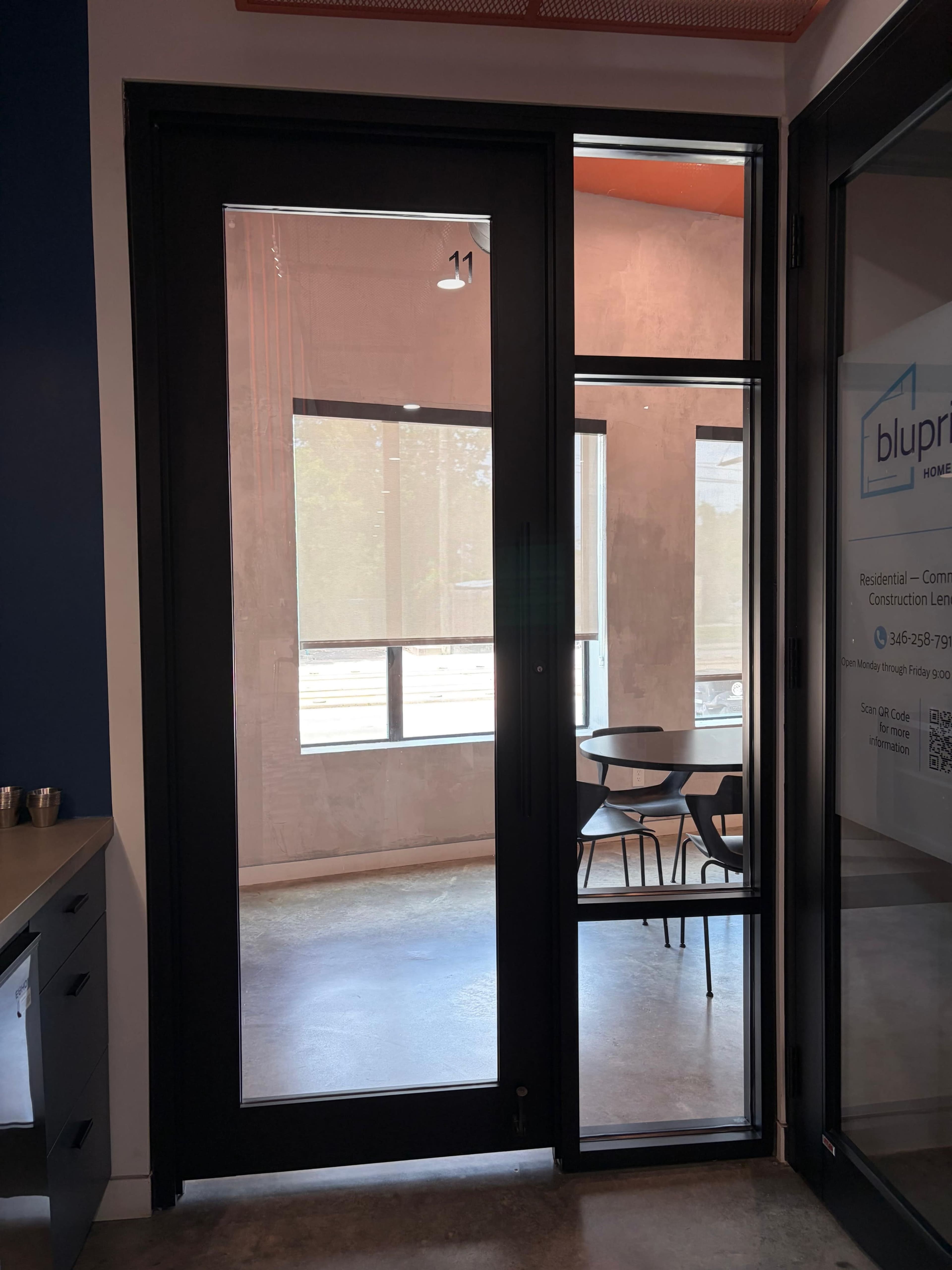 A glass door with a small window pane stands open, revealing a room with a table and chairs in a modern interior setting.