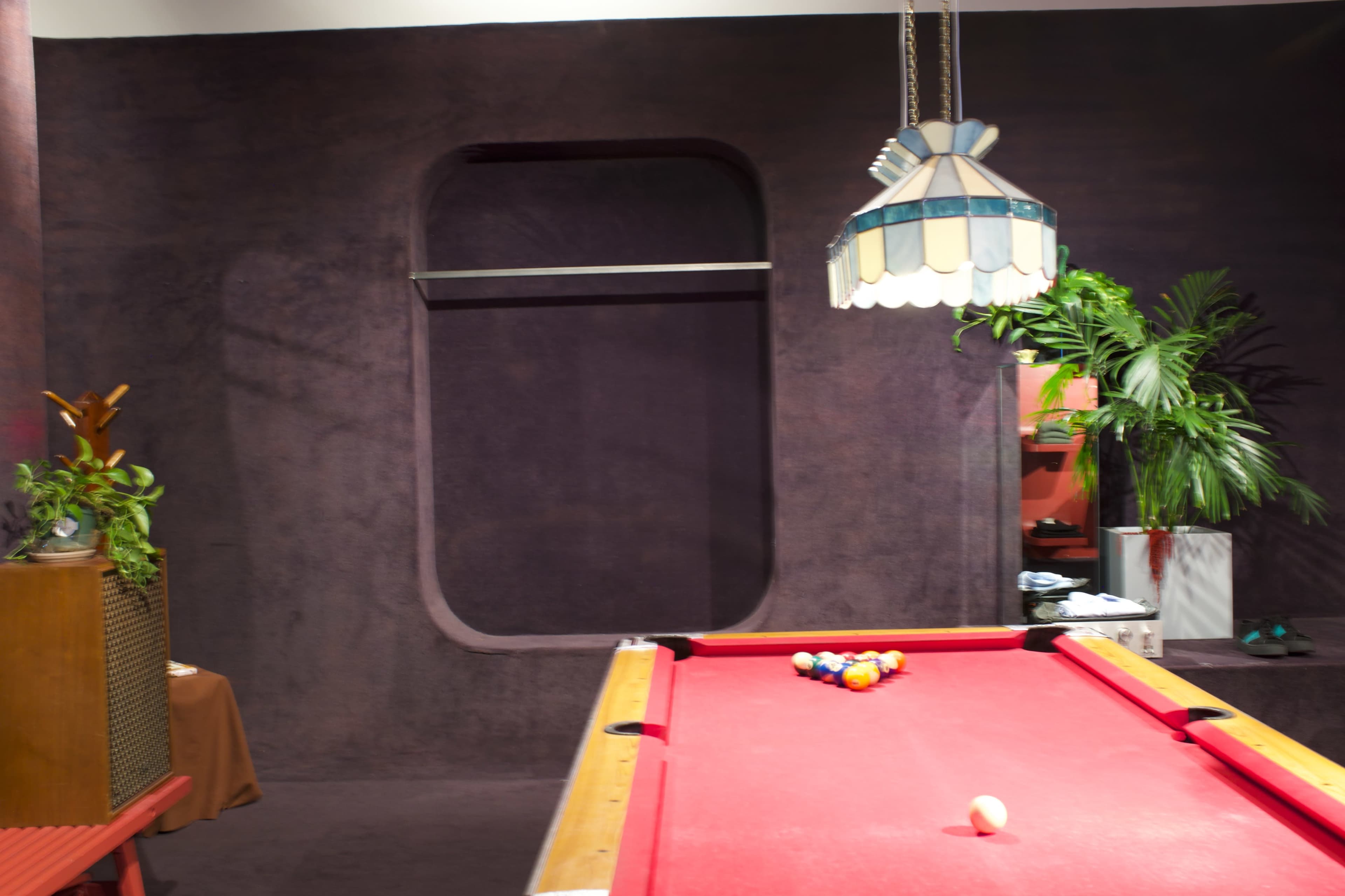 A pool table with balls arranged in a triangle sits in a room featuring purple walls and a hanging light fixture.