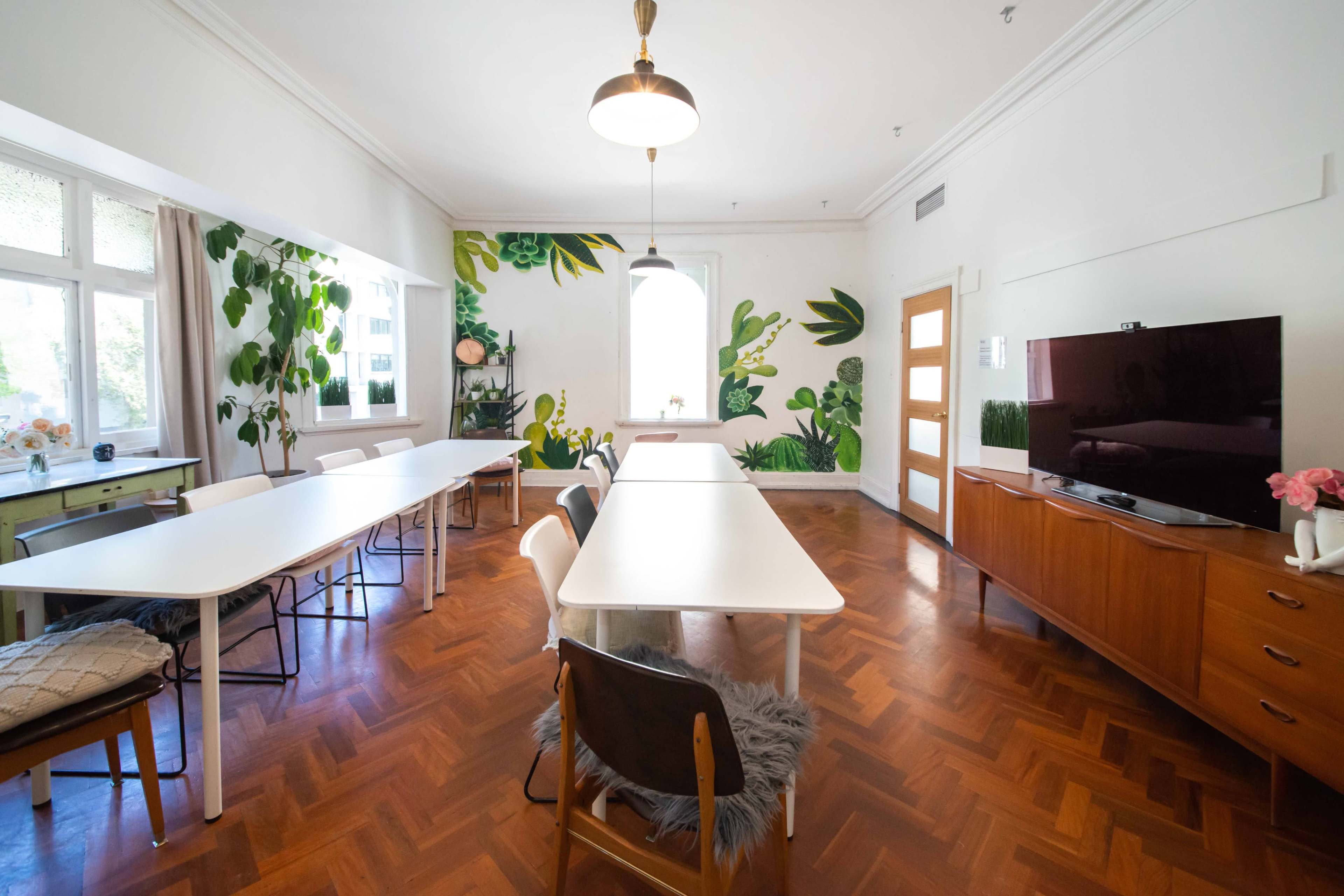 A bright room with large tables, wooden flooring, and green plant-themed wall decorations.