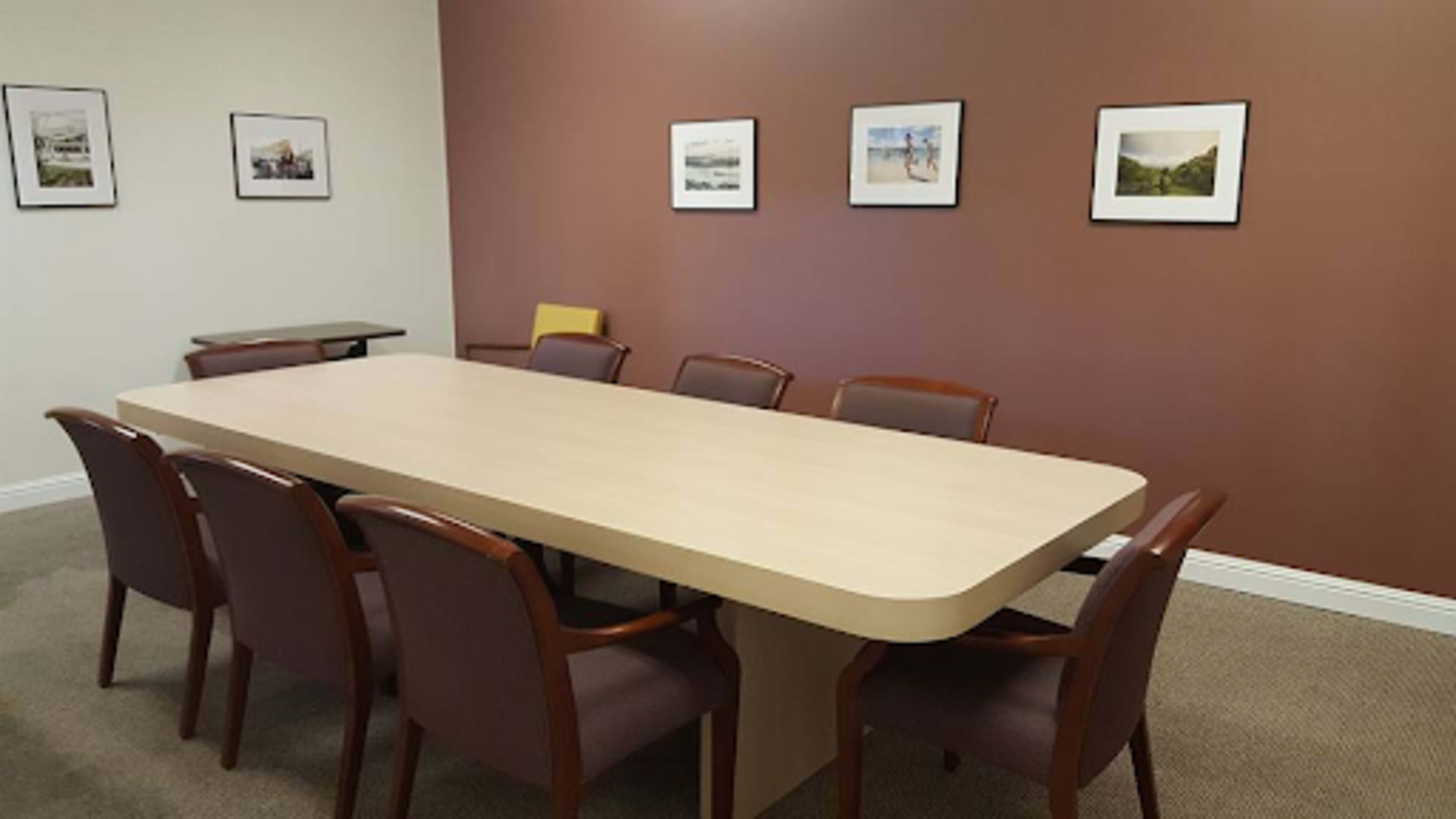 A long wooden table is surrounded by chairs in a meeting room with framed photographs on the walls.