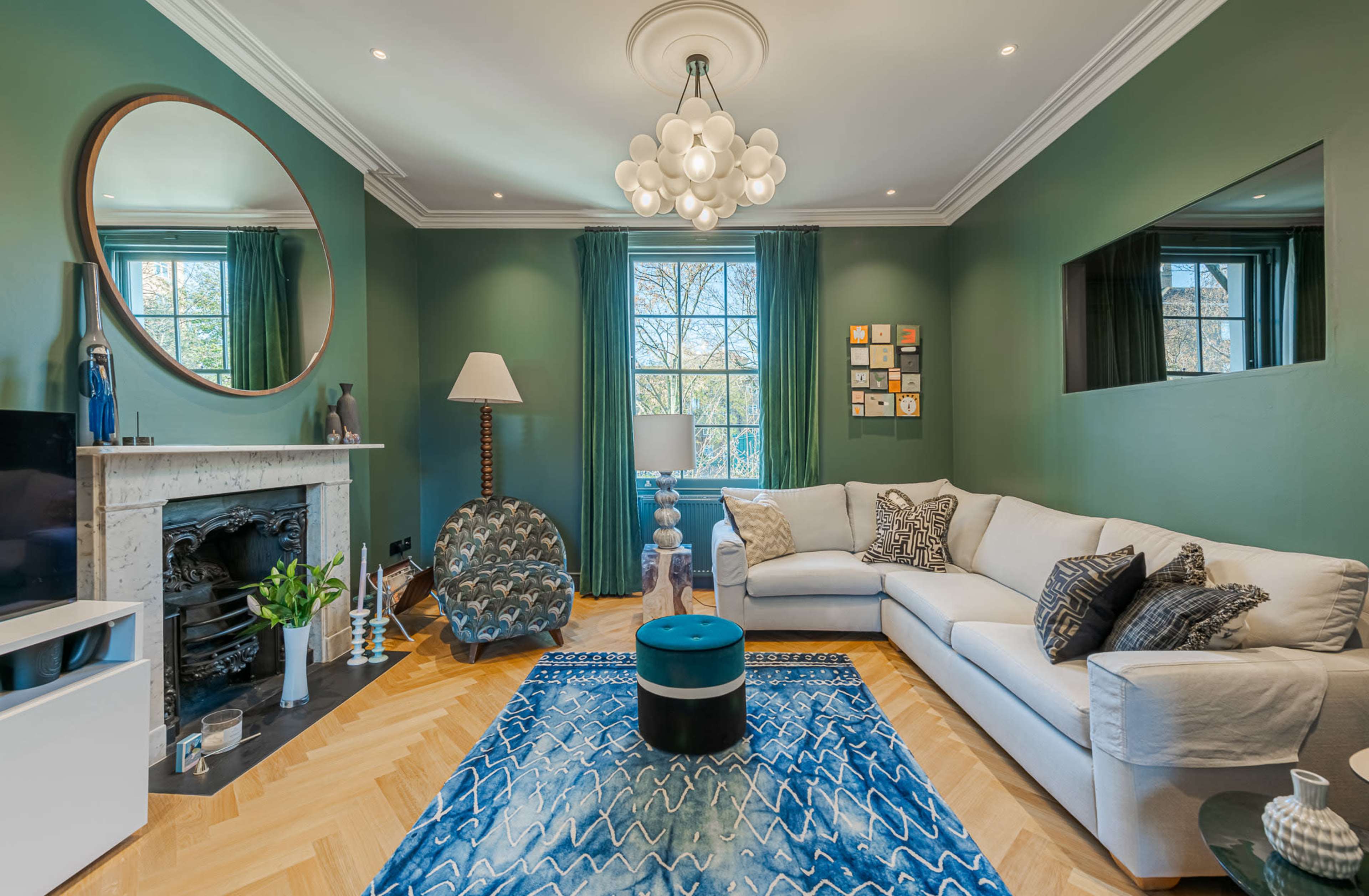 The living room features a white sectional sofa, a blue patterned rug, a large mirror, and a fireplace, complemented by green walls and decorative accents.
