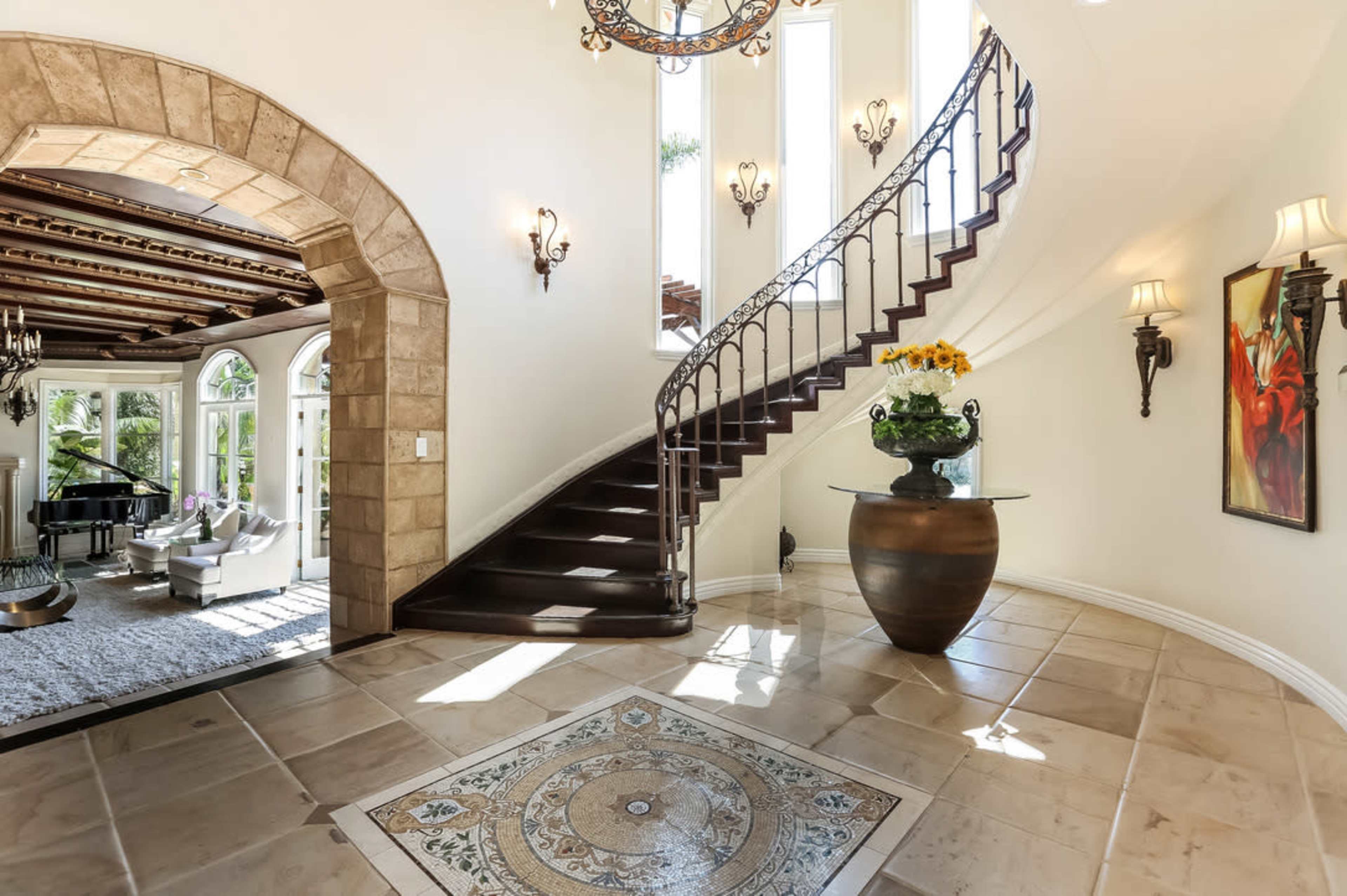 A grand entrance features a curved staircase, ornate ceiling, and a decorative tiled floor.