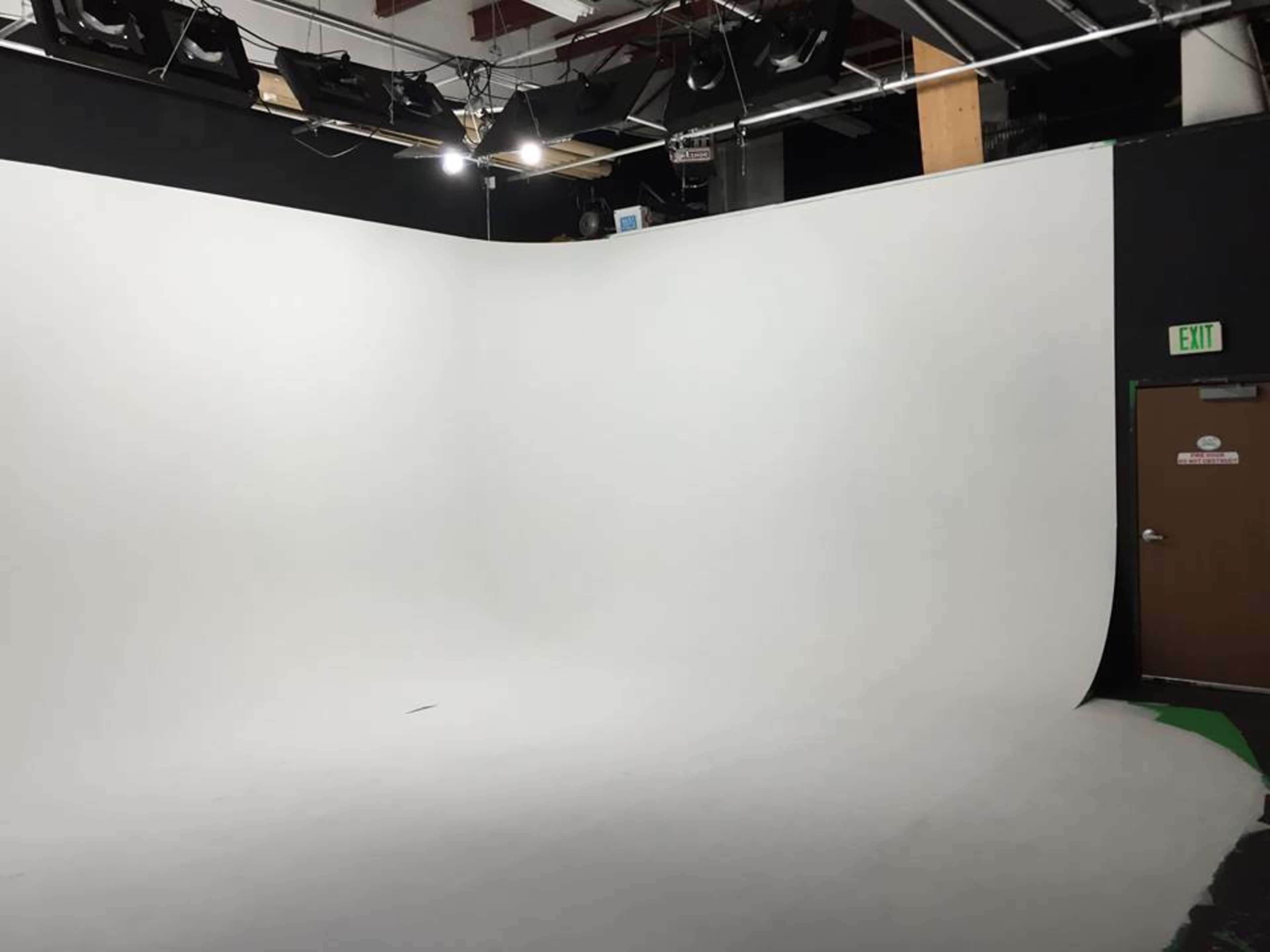A photography studio featuring a seamless white backdrop and various overhead lights.