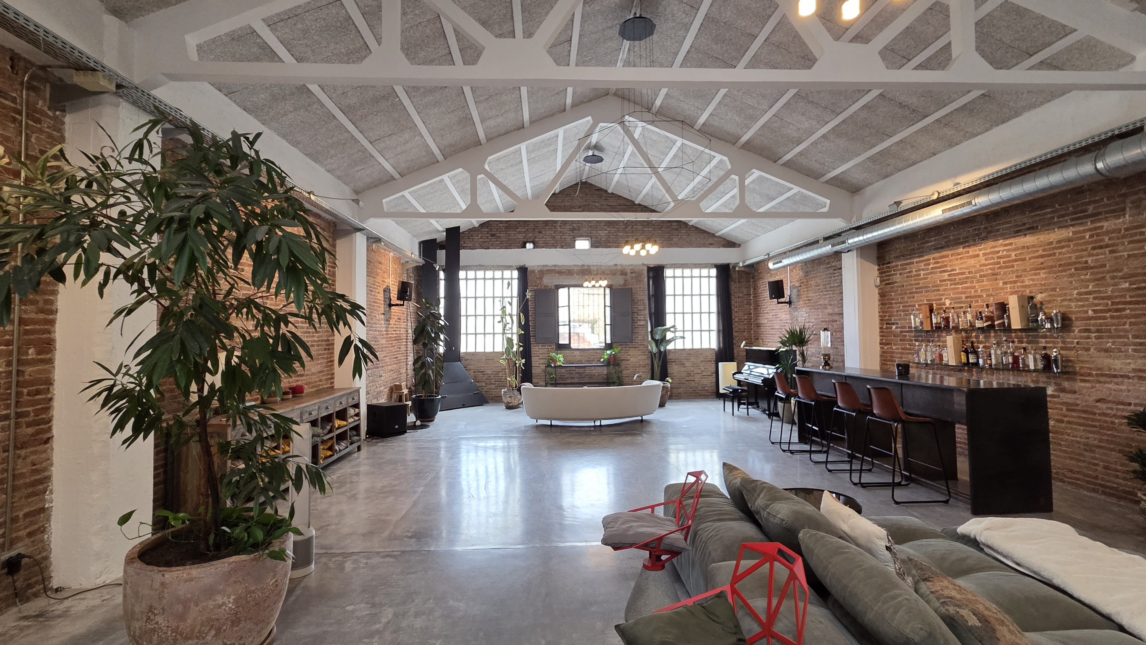The image shows a spacious interior of a modern loft with exposed brick walls, high ceilings, and a bar area.