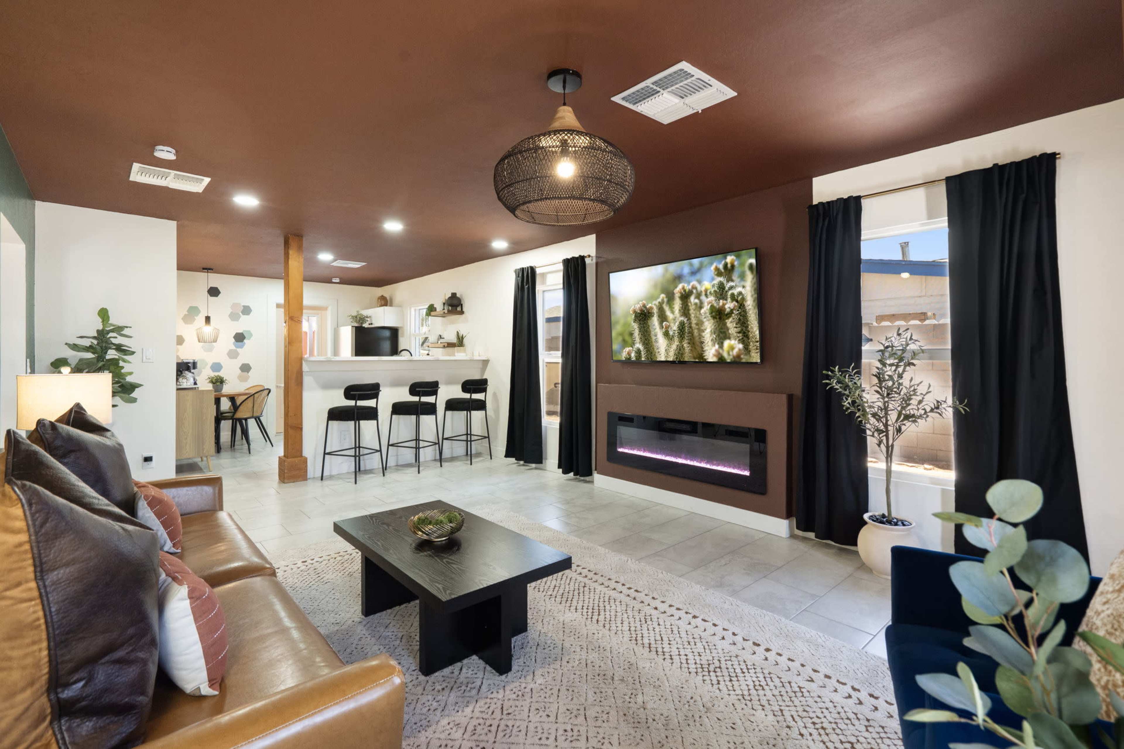 The image features a modern living room with a brown accent wall, a black coffee table, a seating area with a brown leather sofa, and a kitchenette in the background.