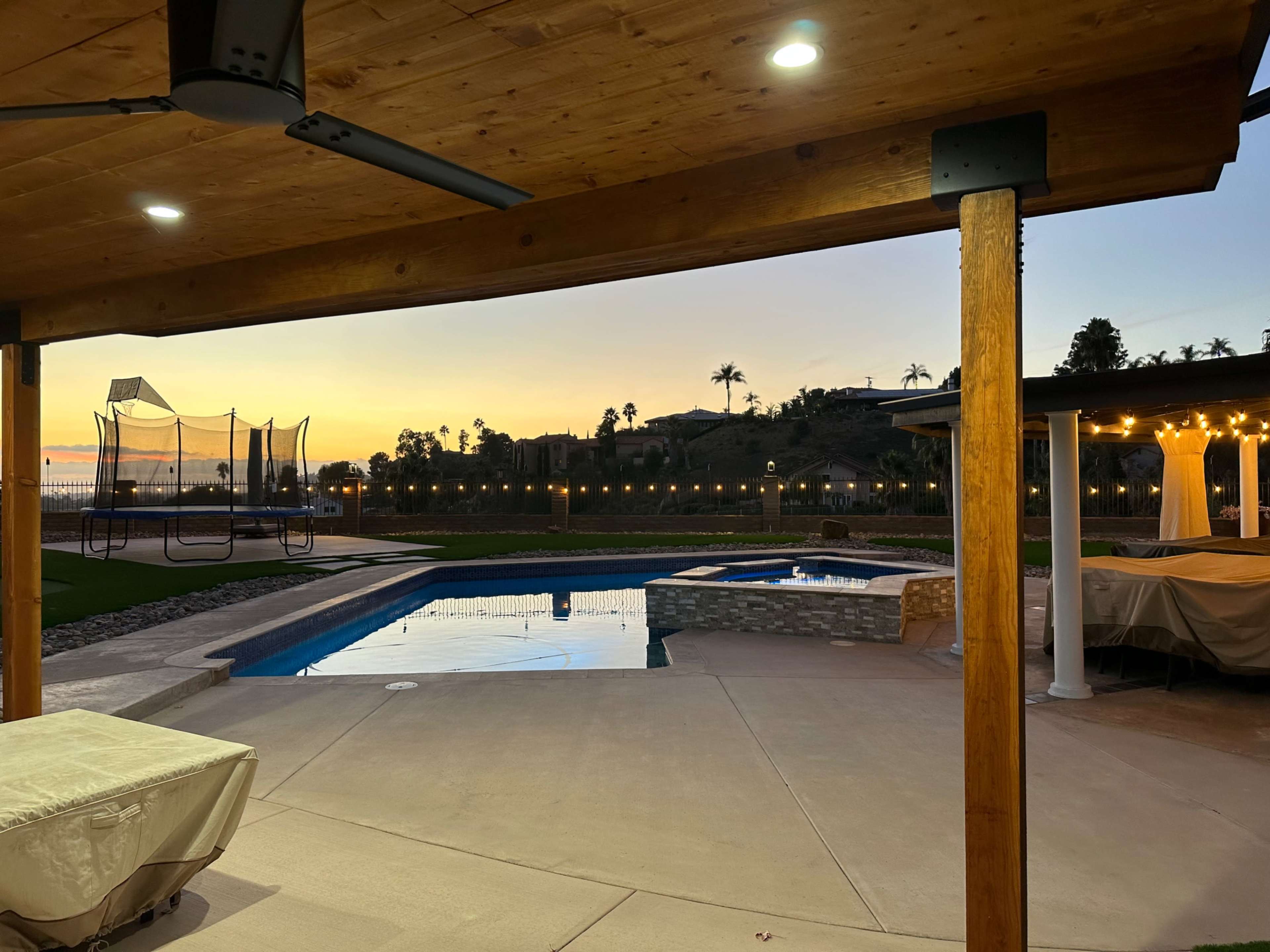 A patio area with a swimming pool and a view of a sunset over a landscaped yard.