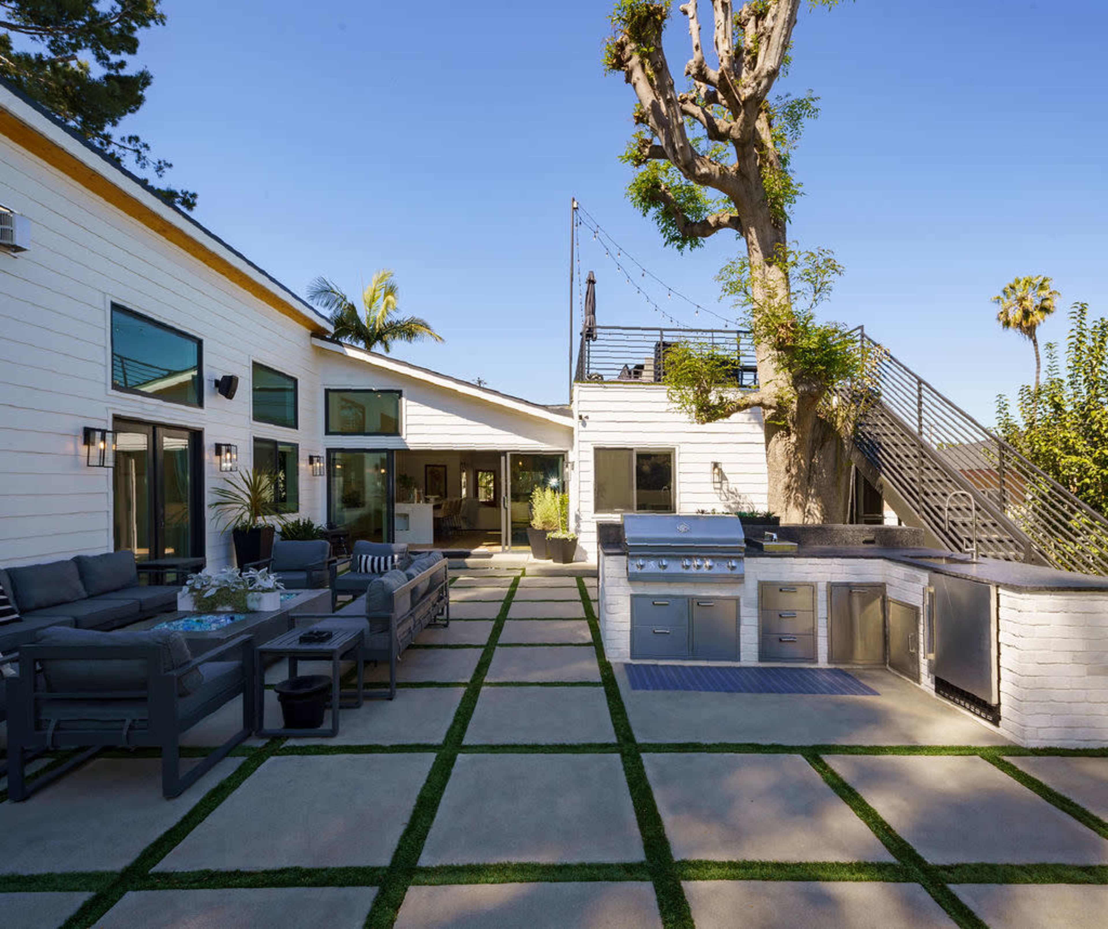 A modern outdoor patio with seating, a barbecue grill, and a landscaped stone pathway.