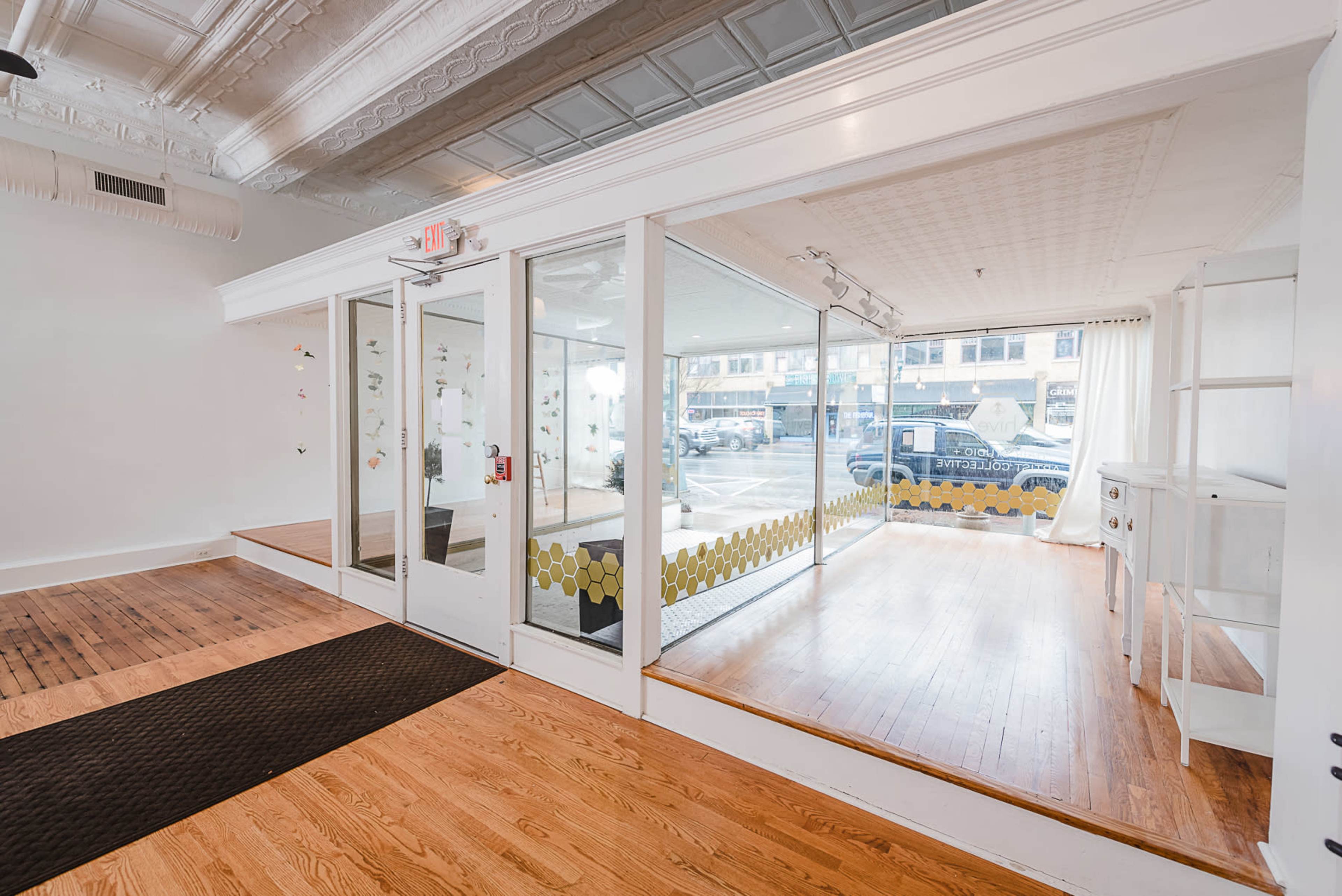 A bright, modern interior of a shop with wooden flooring, large glass windows, and a small display area.