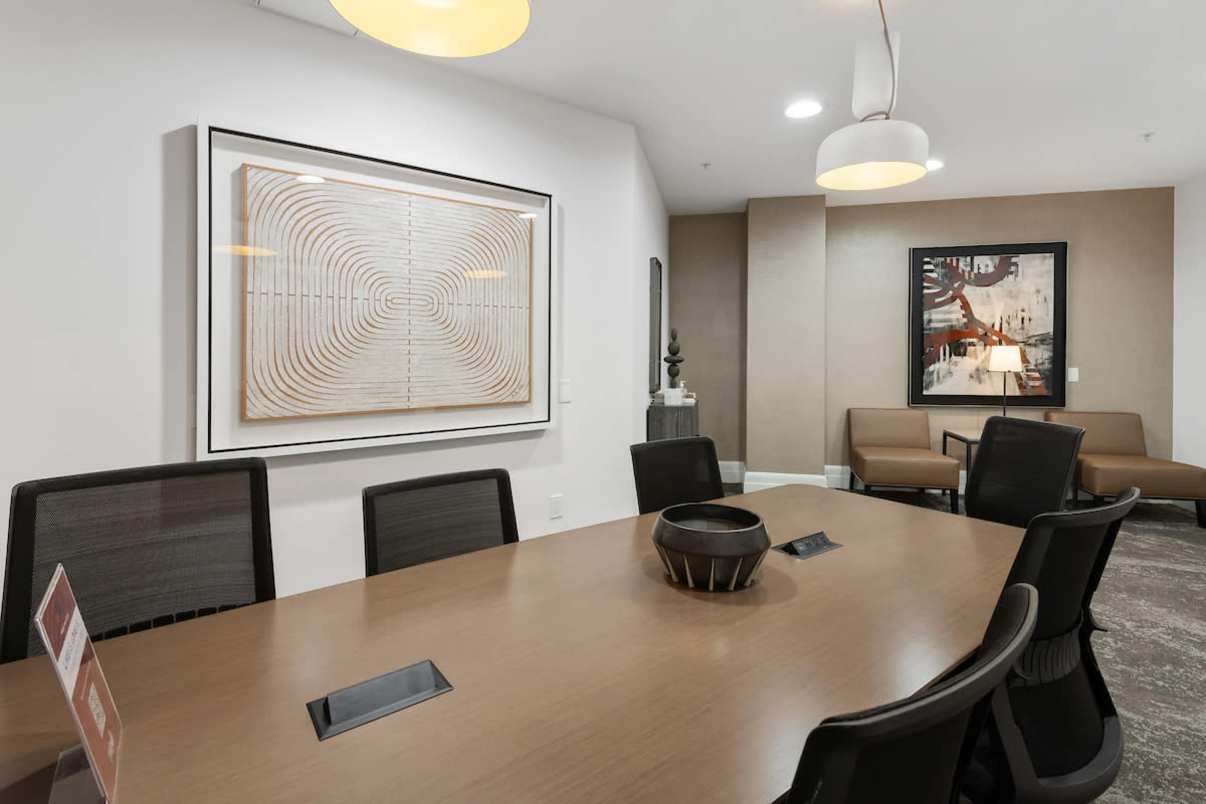 A modern conference room features a large wooden table surrounded by black chairs, with artwork and a decorative bowl on display.